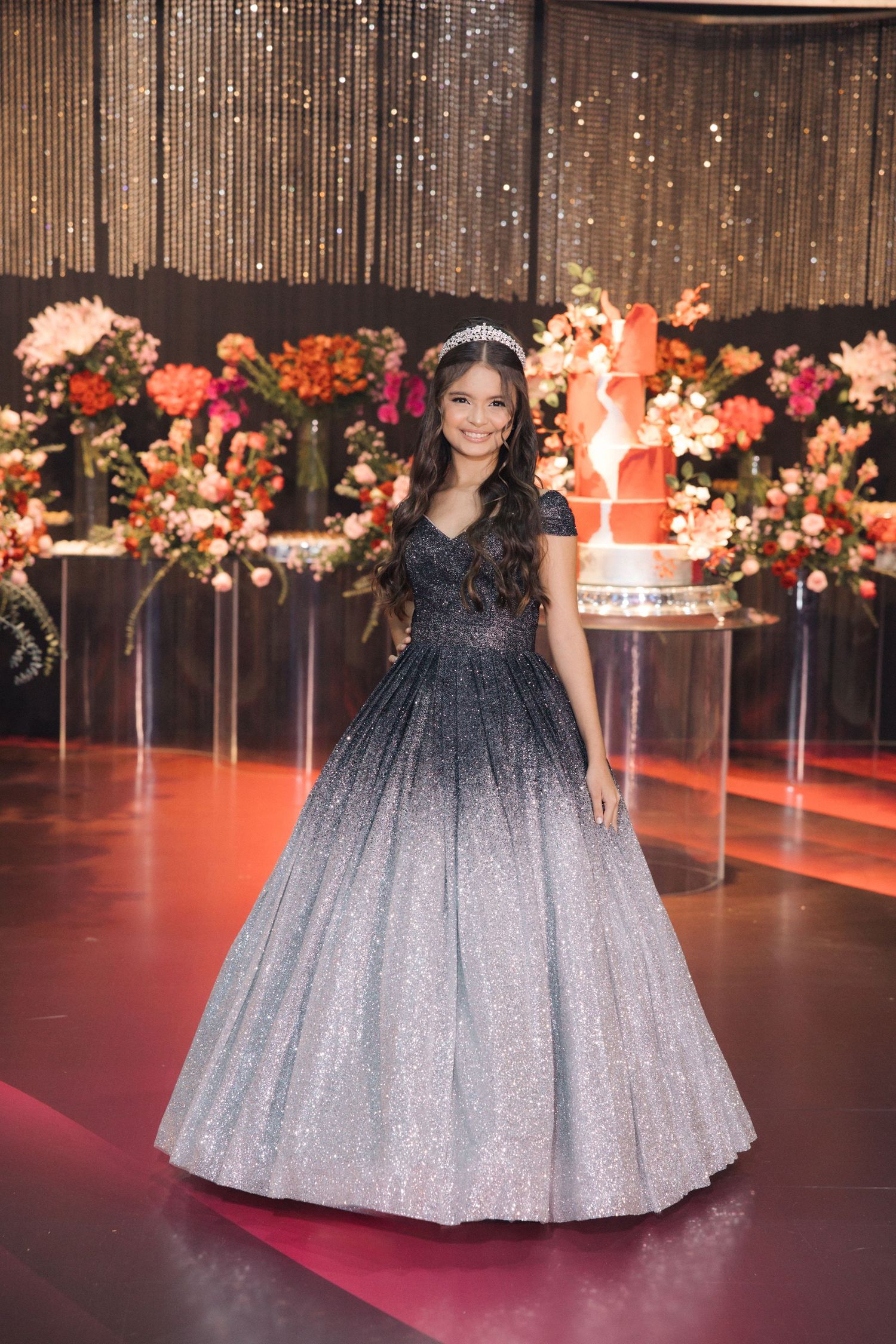 A sparkling ombre ball gown in navy and silver worn at an elegant event with floral decorations and a tall cake.