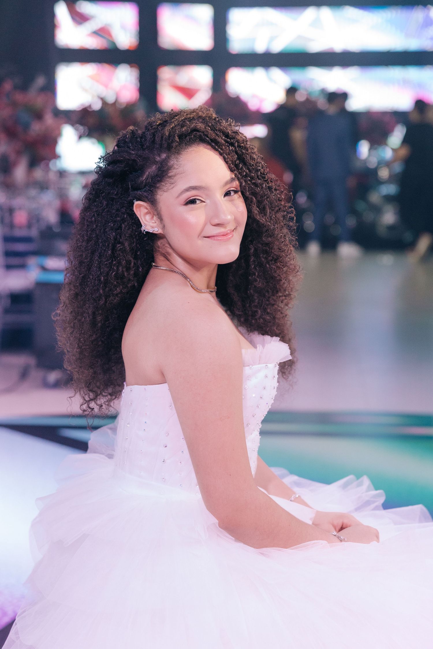 An elegant strapless white ballgown photographed in a venue with colorful lights in the background.