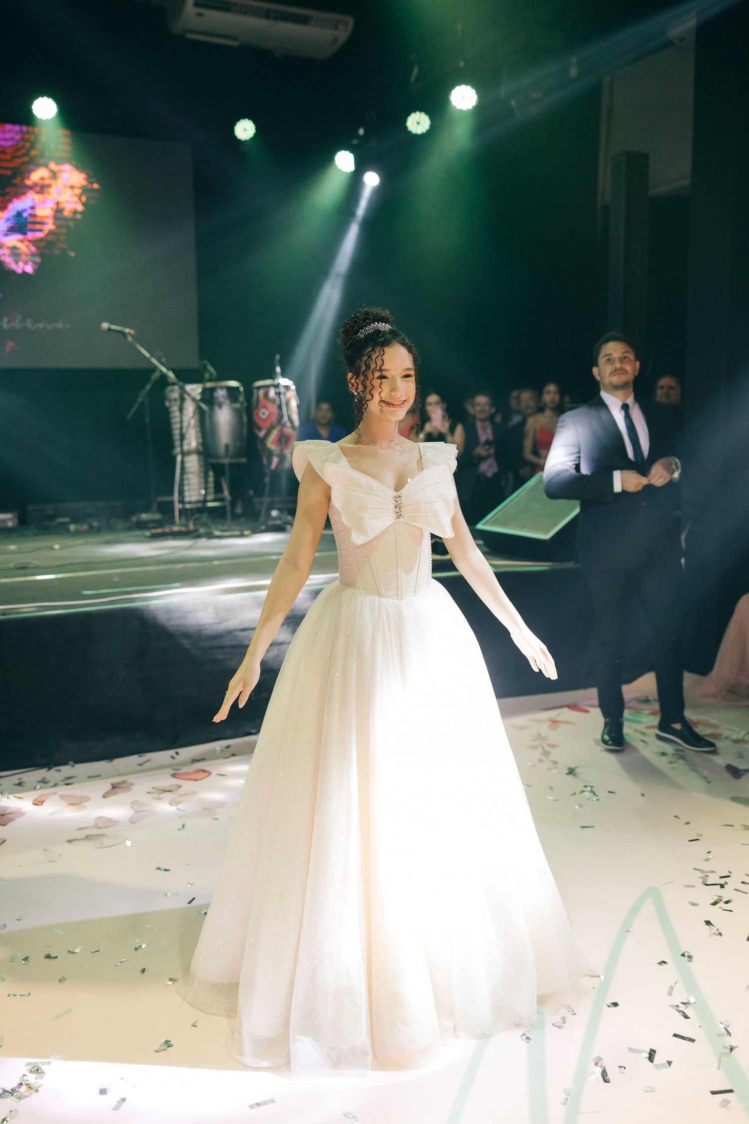 A bride in a white gown stands on stage under dramatic green lighting during a wedding reception.