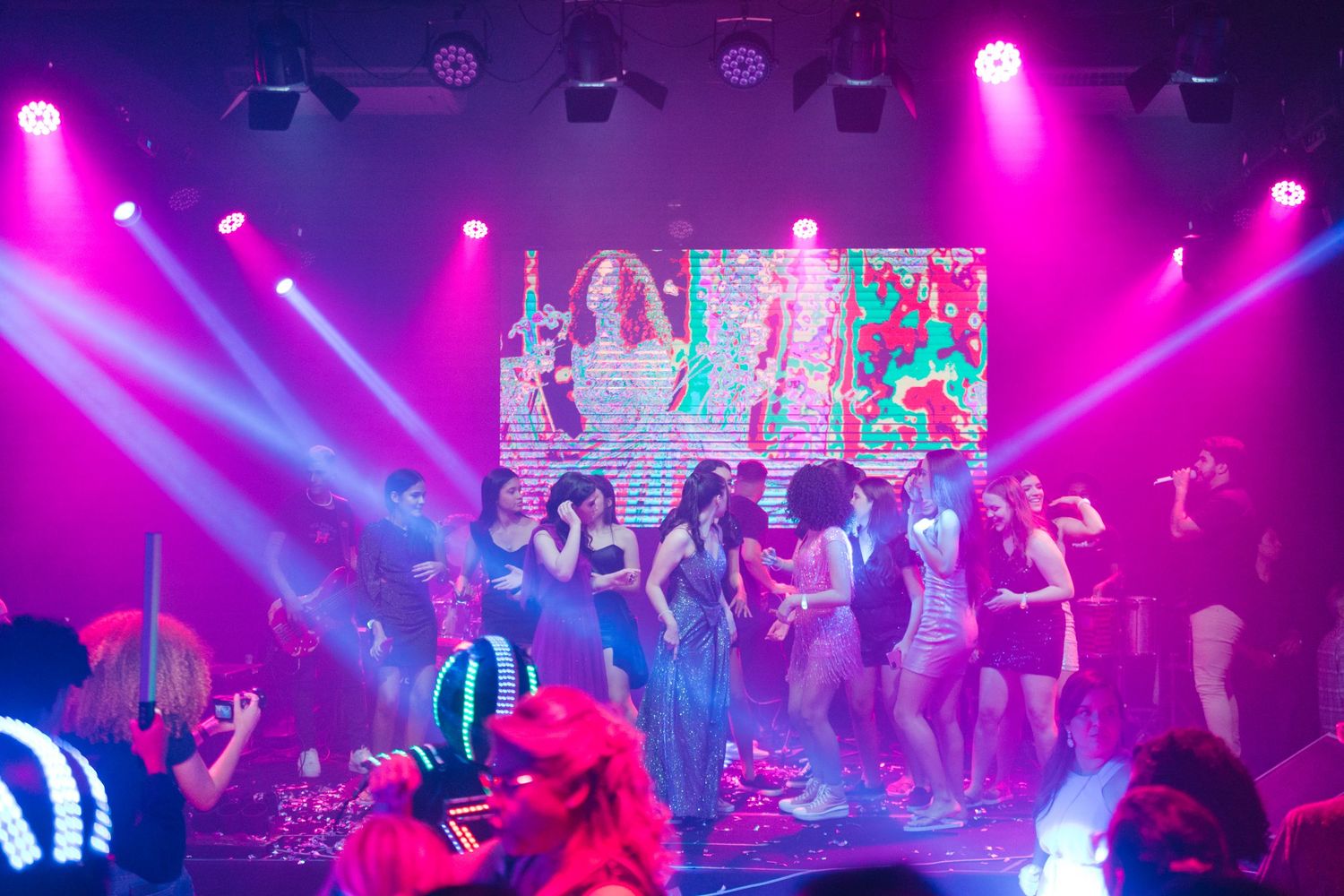 Nightclub dance party with vibrant pink and blue lighting and people dancing on a crowded floor.