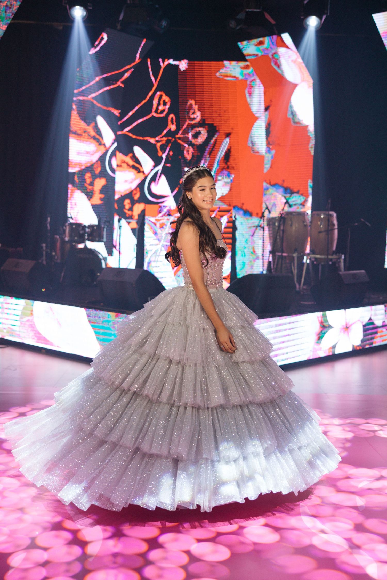 Silver tiered ball gown twirling on illuminated pink dance floor with colorful digital backdrop.