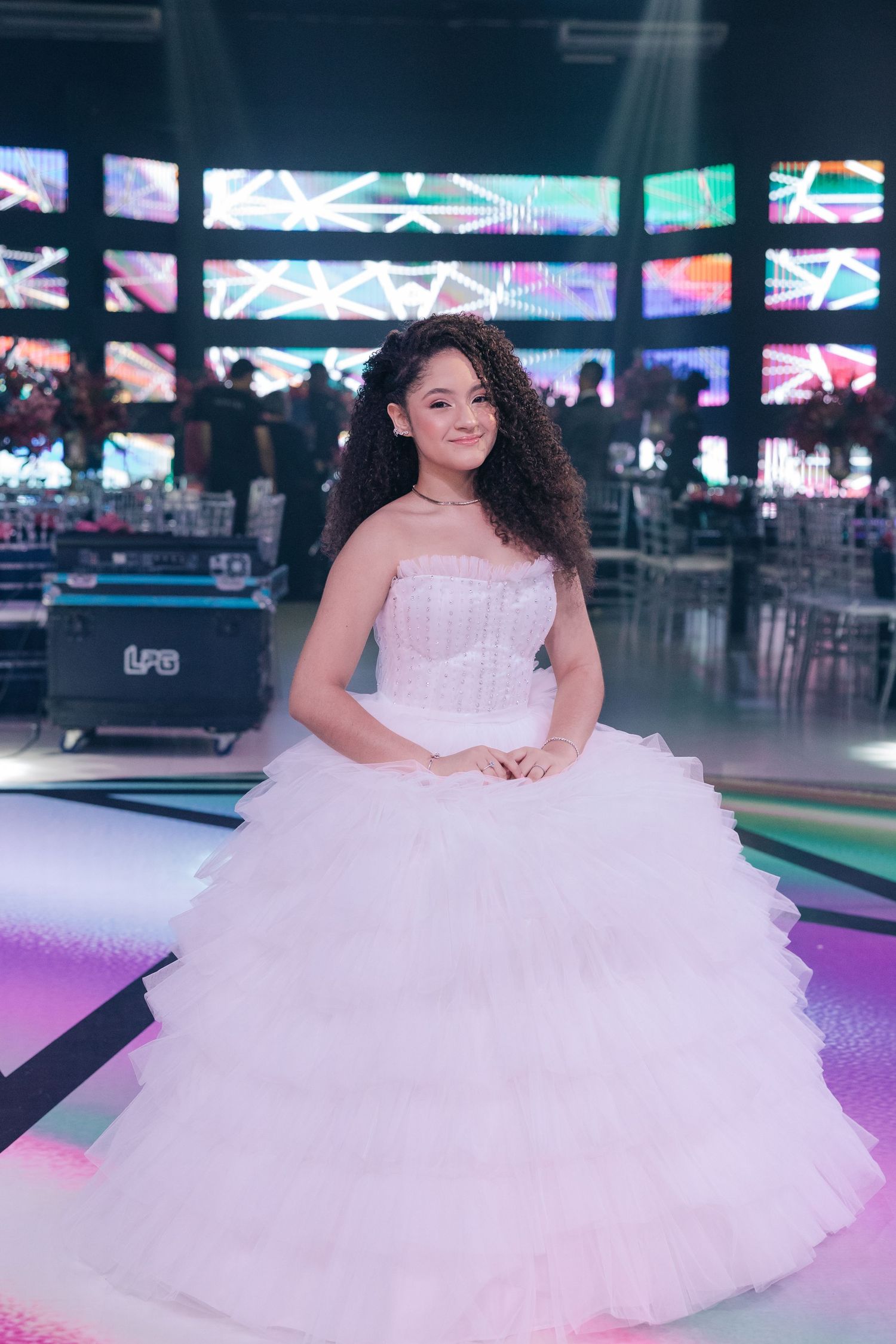 A white tulle quinceañera dress showcased in a modern venue with LED screen walls.