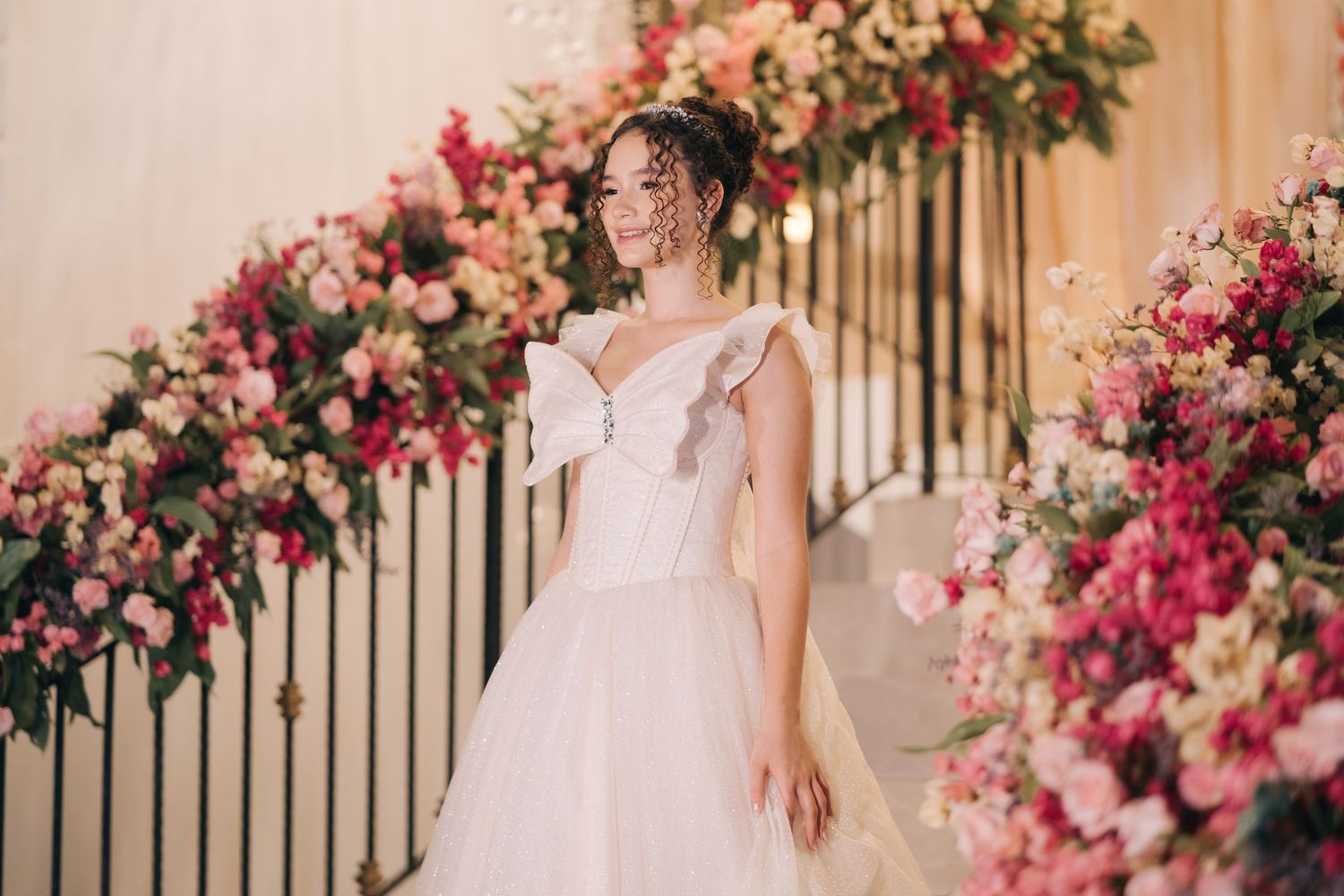 Side profile of bride in romantic white gown posed against pink floral staircase decor.