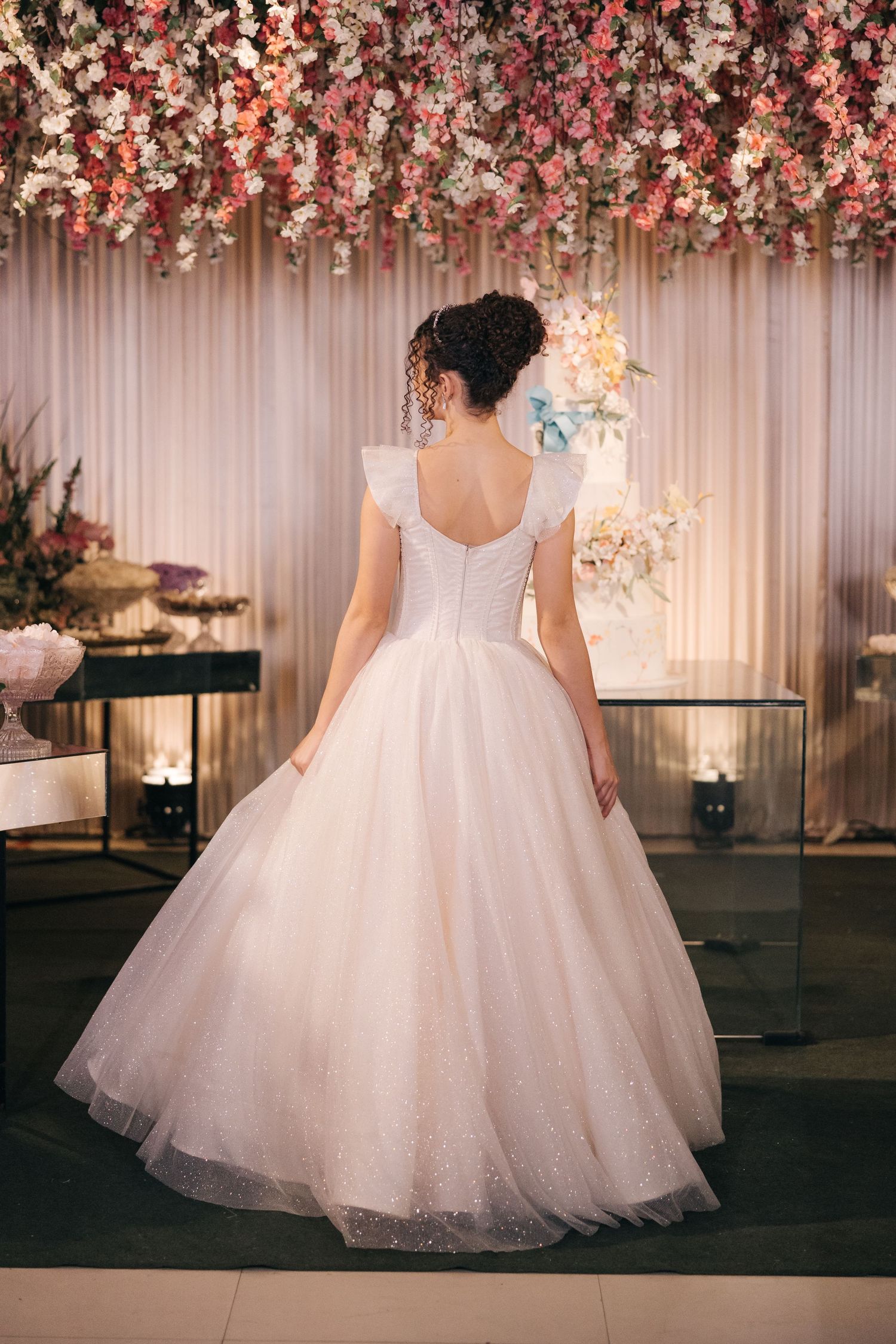 Back view of wedding dress showing elegant details against floral backdrop with hanging blossoms.