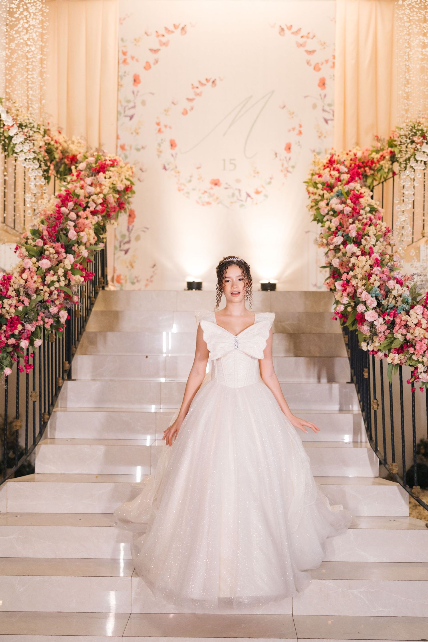 Elegant wedding setup with white stairs adorned by pink and cream floral arrangements leading to an illuminated circular backdrop.