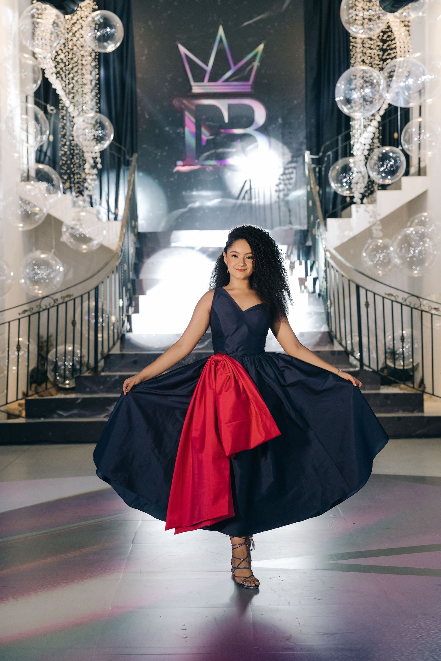 A figure twirls in a dramatic navy and red dress on a grand staircase adorned with crystal decorations.