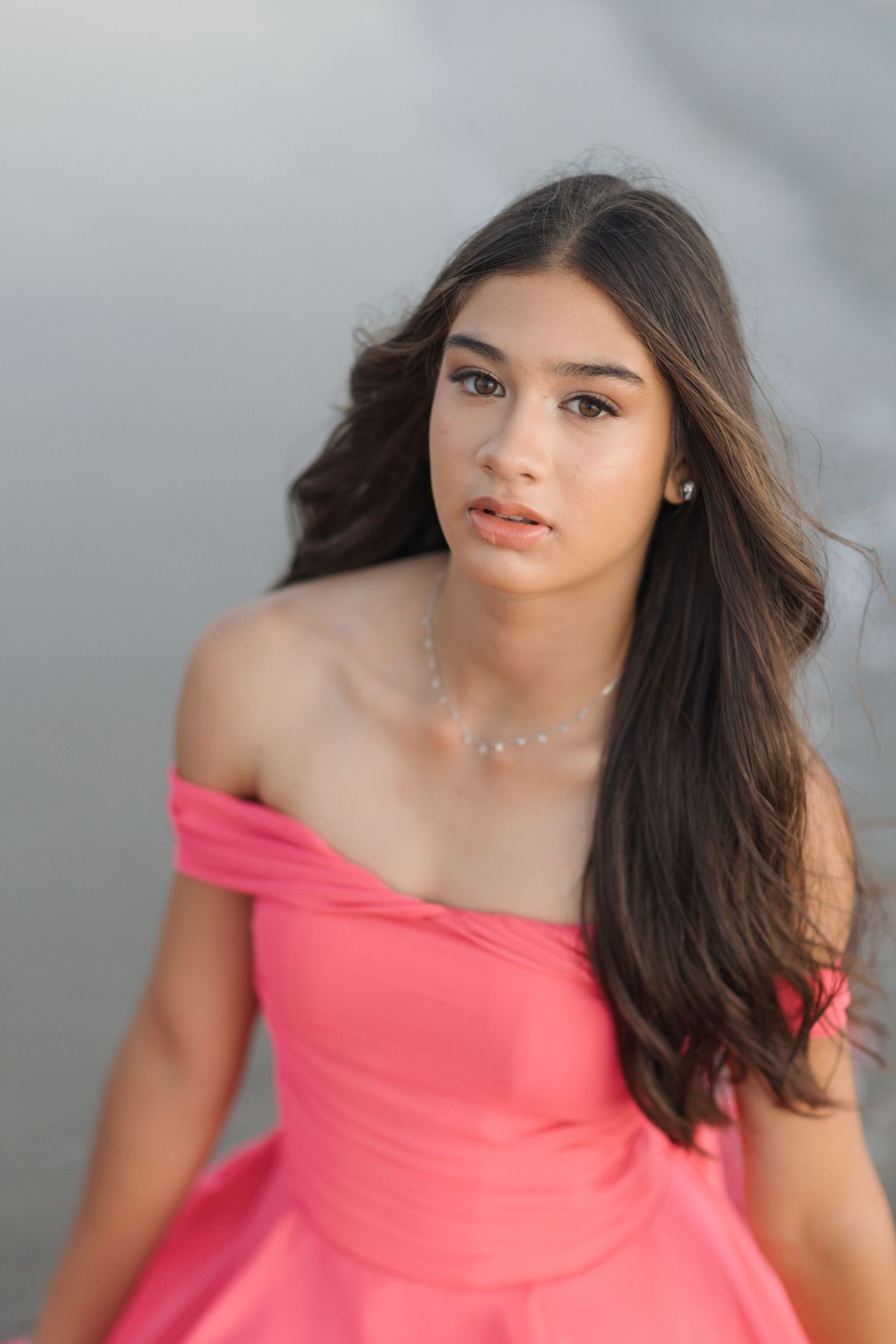 Off-shoulder coral pink dress captured in soft portrait lighting against neutral background.