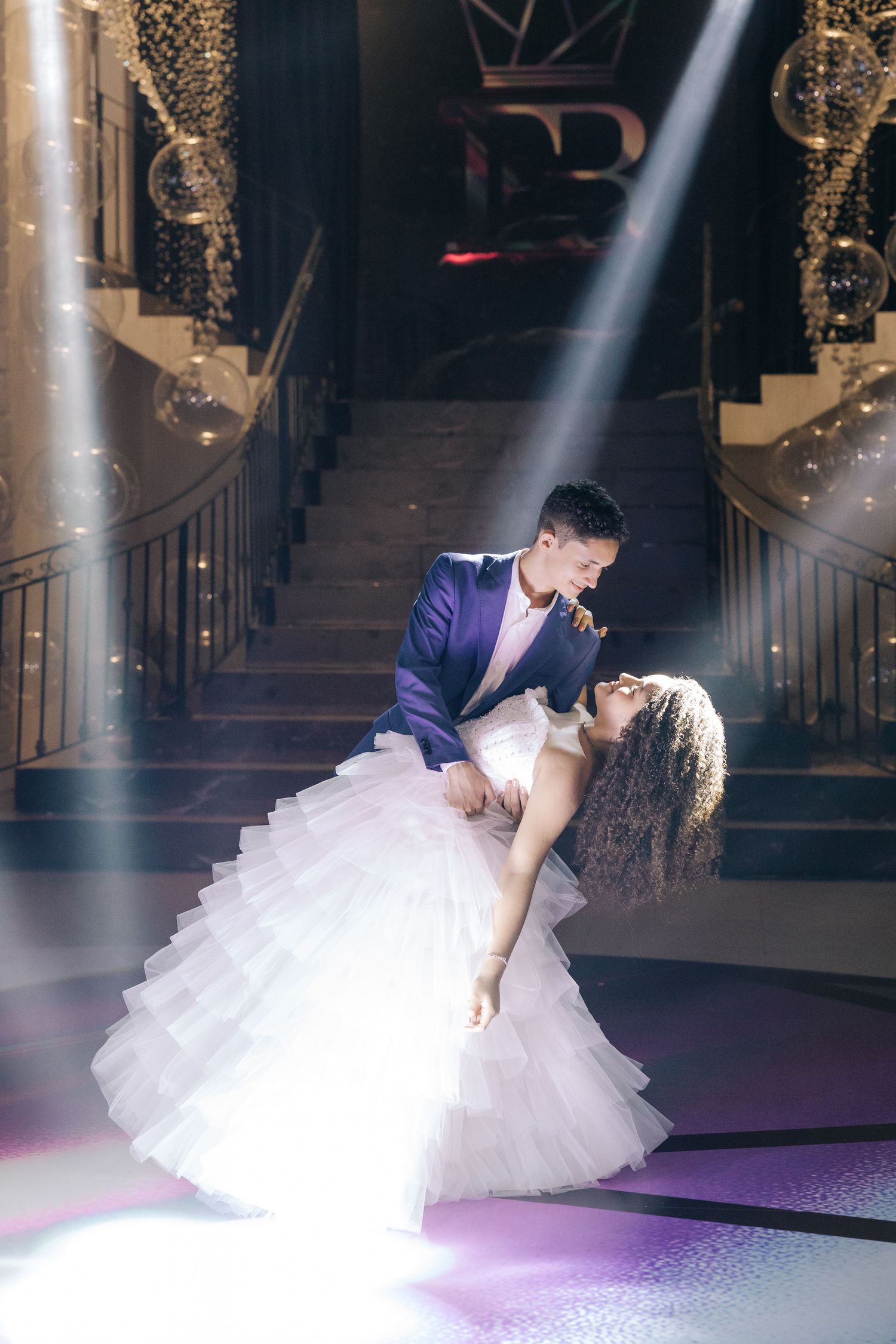 A romantic dance dip captured under dramatic spotlighting on an elegant staircase.