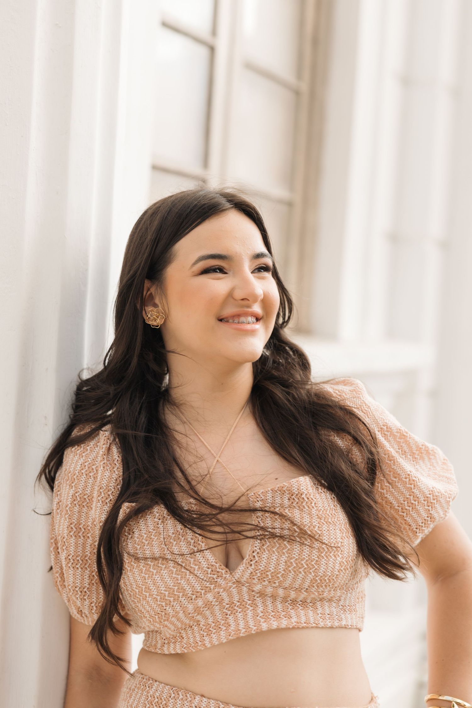 Portrait of someone in a peach-colored knit crop top by white columns smiling warmly in natural light.