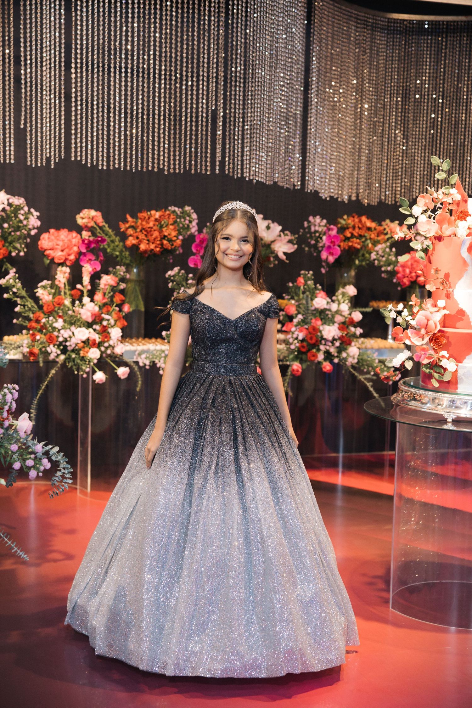 A glamorous black and silver ball gown photographed against a backdrop of glittering beads and flowers.