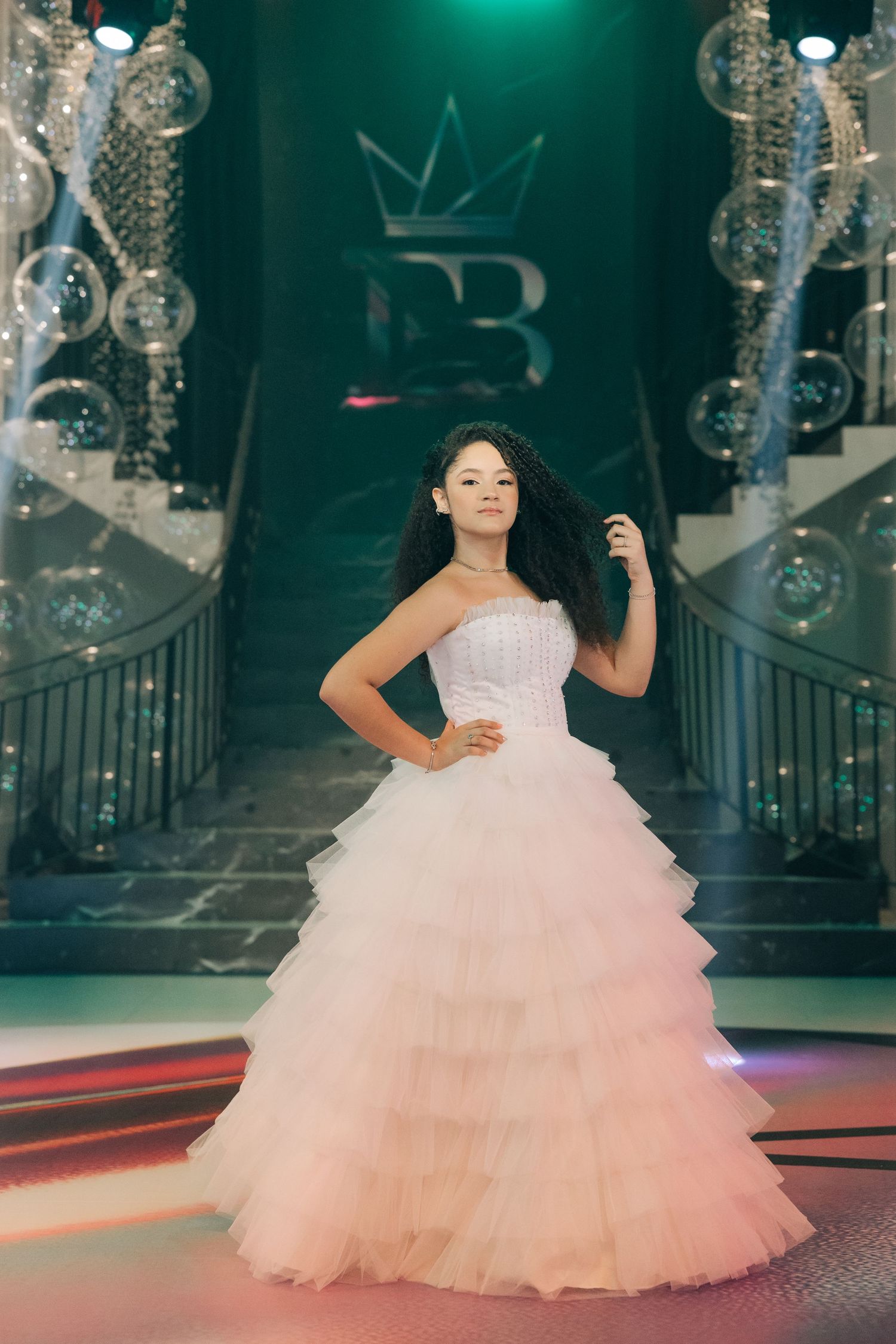 An elegant white layered tulle gown displayed in a venue with dramatic lighting and decorative elements.