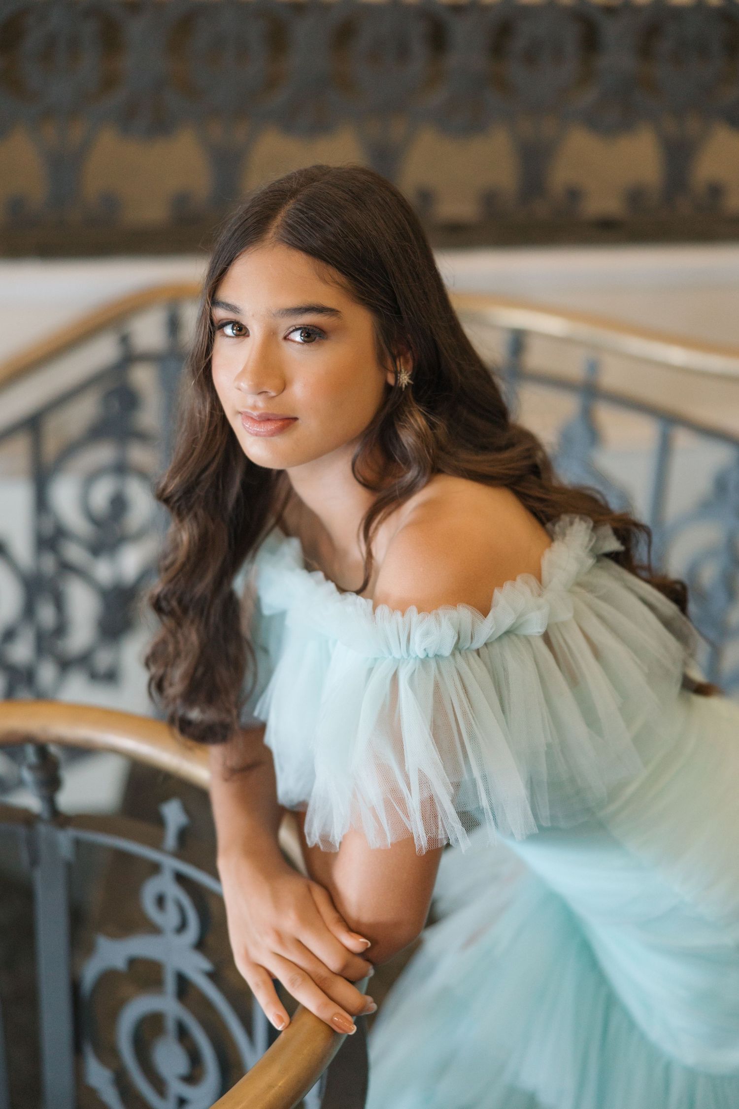 A delicate off-shoulder mint gown with ruffled details is captured against an ornate staircase railing.