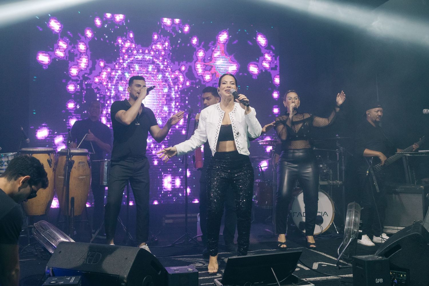 Concert performers on stage with purple heart-shaped lighting effects and backup dancers in the background.