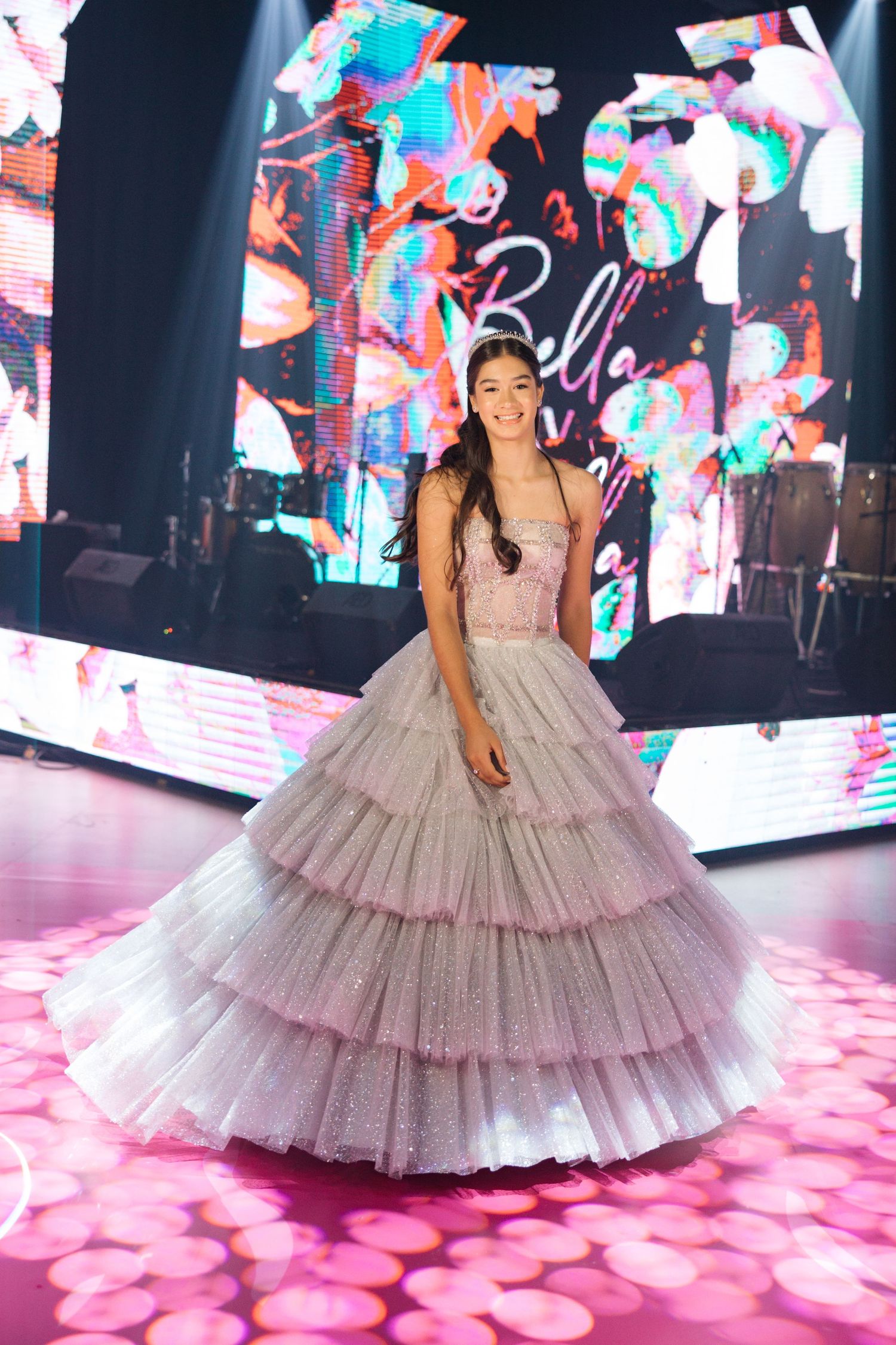 A stunning ball gown against colorful digital displays and pink lighting on a performance stage.