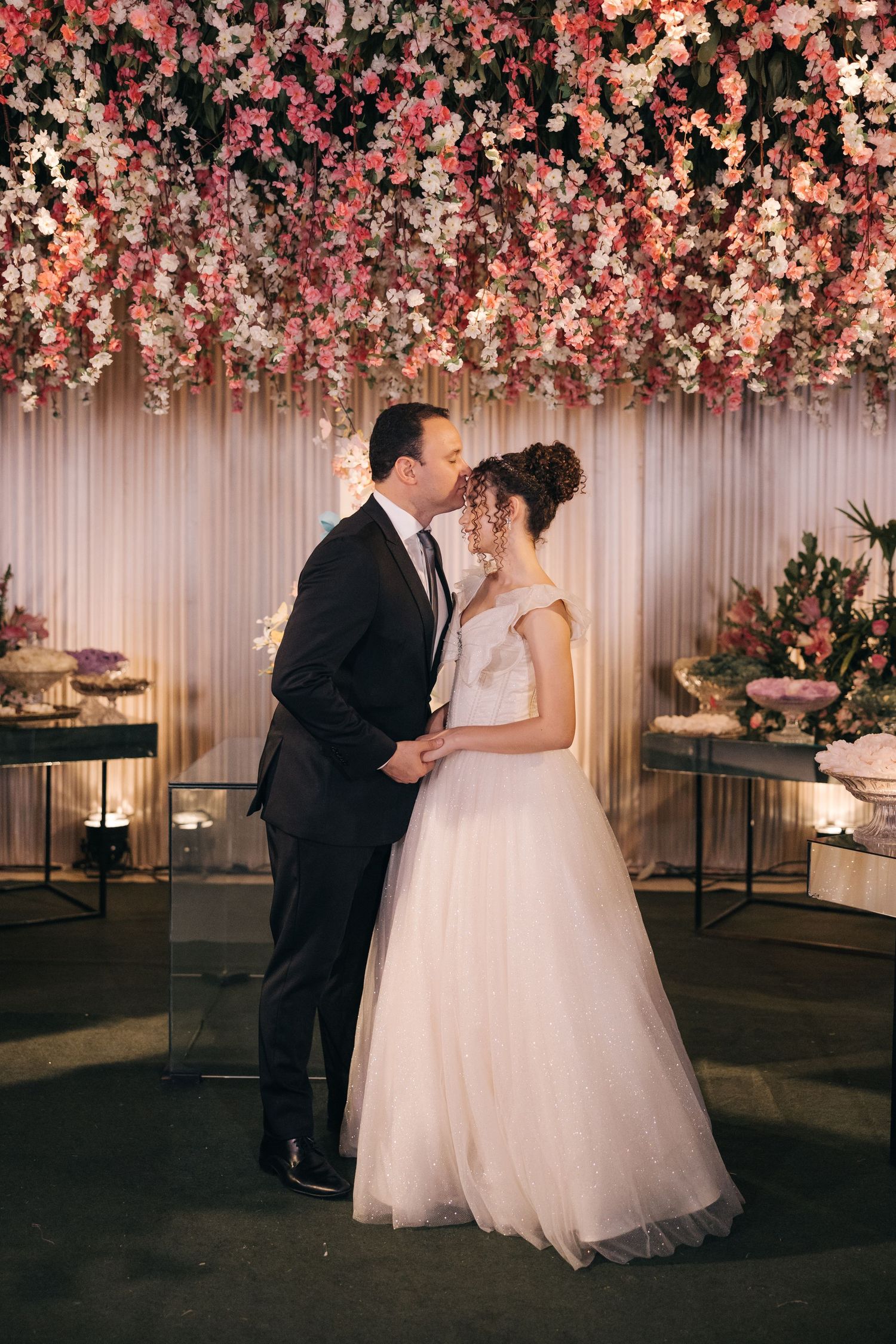 Romantic wedding moment under cascading pink and white floral ceiling installation.