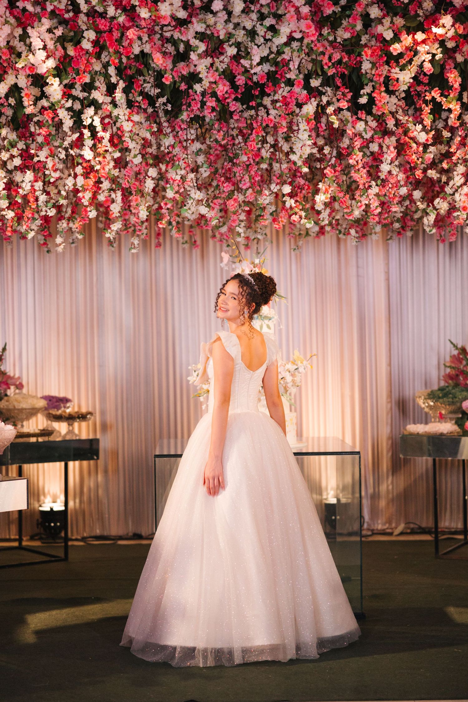 Elegant wedding setup with cascading pink and white floral ceiling installation and tulle ballgown against draped backdrop.