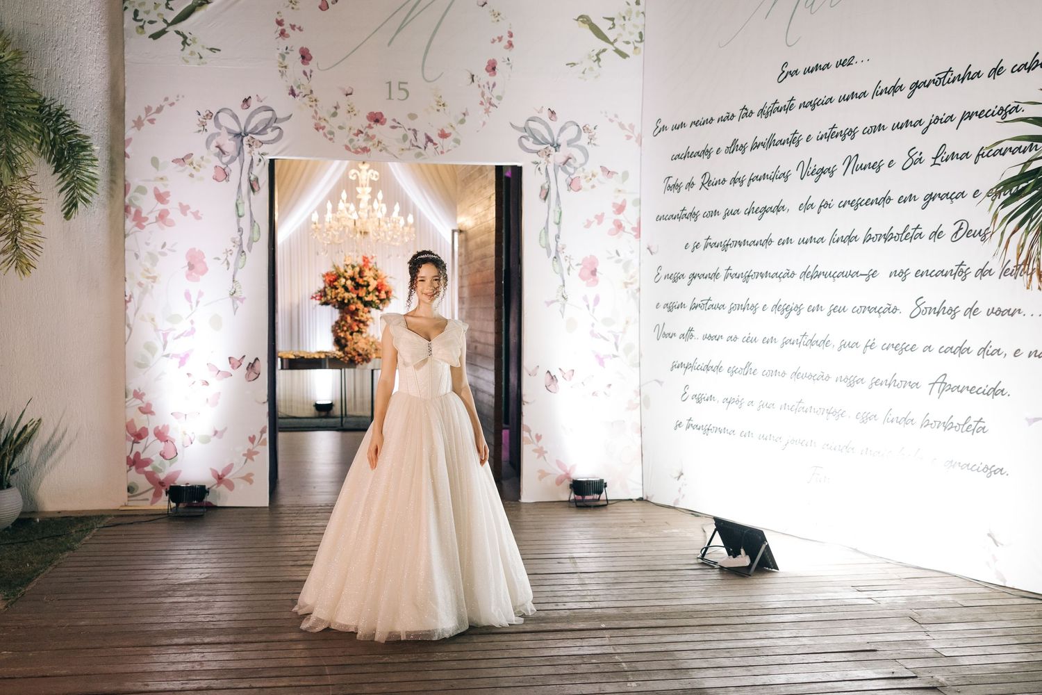 A person in a flowing white wedding gown stands elegantly in a room with floral walls and decorative text.
