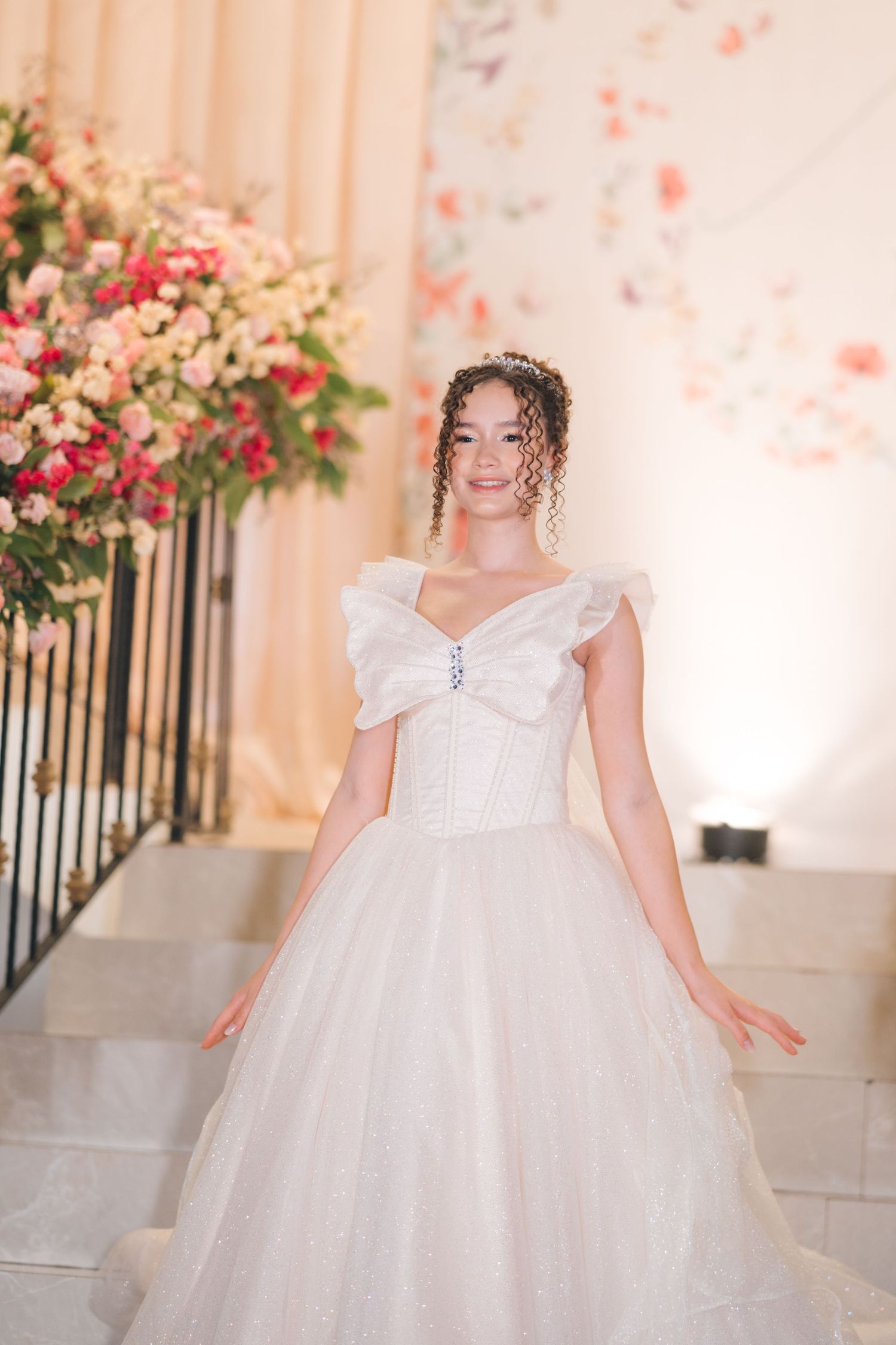Ethereal white wedding gown with ruffled cap sleeves displayed against soft pink floral decor.
