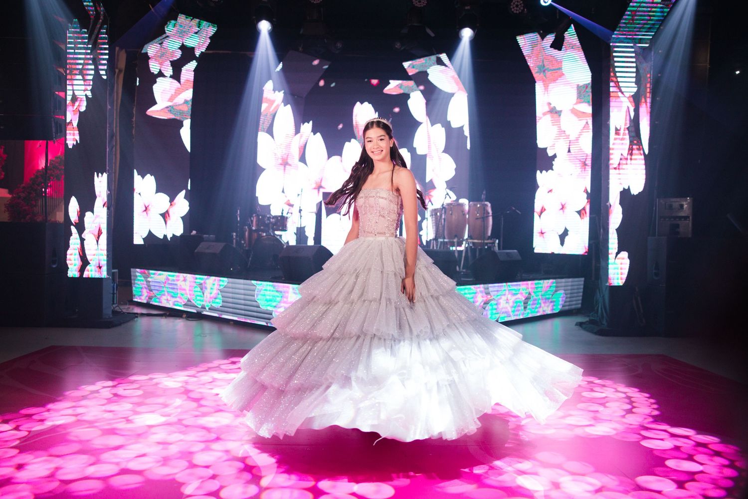 A stunning quinceañera celebration with a princess ball gown illuminated by pink lighting and butterfly decorations on LED screens.