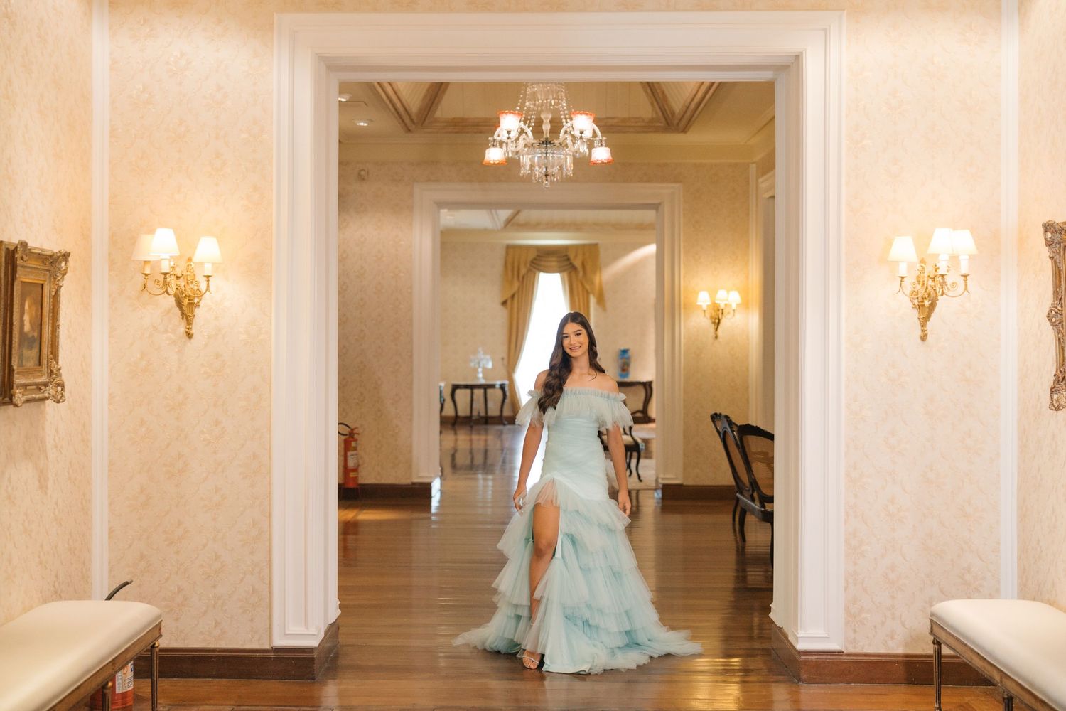 Light turquoise formal gown captured in a luxurious hallway with crystal wall sconces and decorative molding.