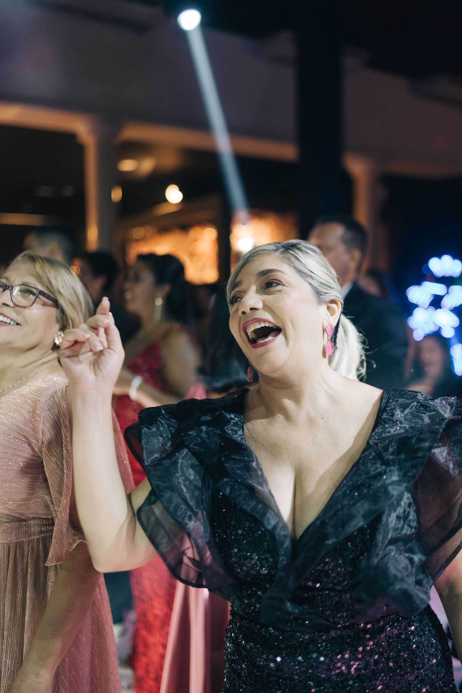 Wedding guests dance and celebrate joyfully under spotlights at an evening reception.