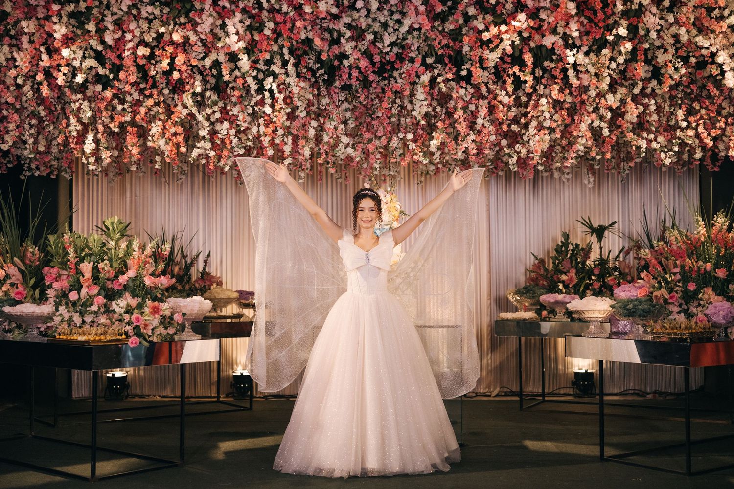 Wedding gown silhouette captured beneath stunning pink floral ceiling installation in reception space.