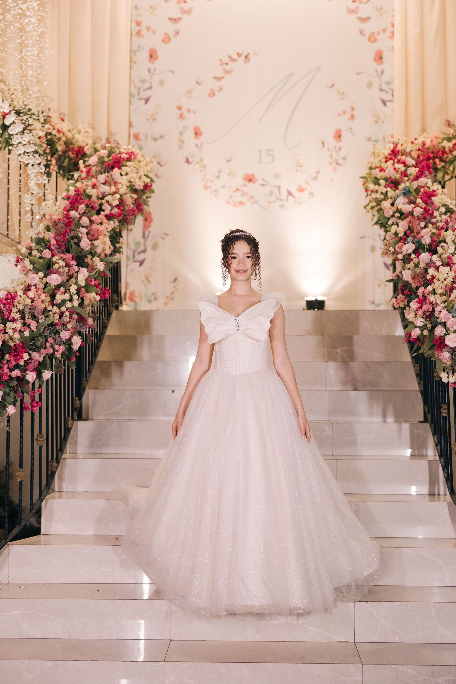 Bride in princess ballgown stands on grand staircase decorated with pink and white floral arrangements.