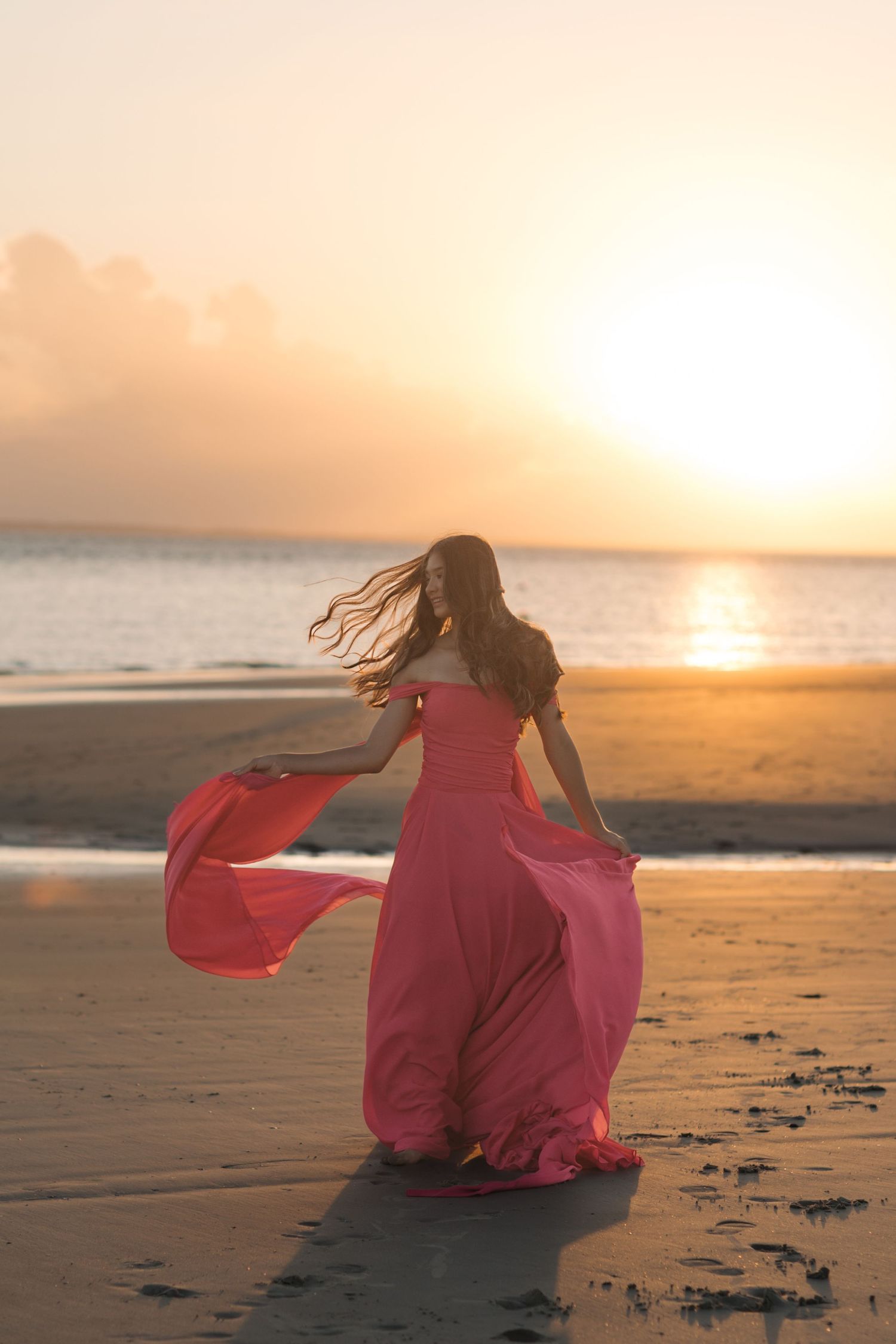 Flowing coral dress billowing in the wind during sunset on a beach.