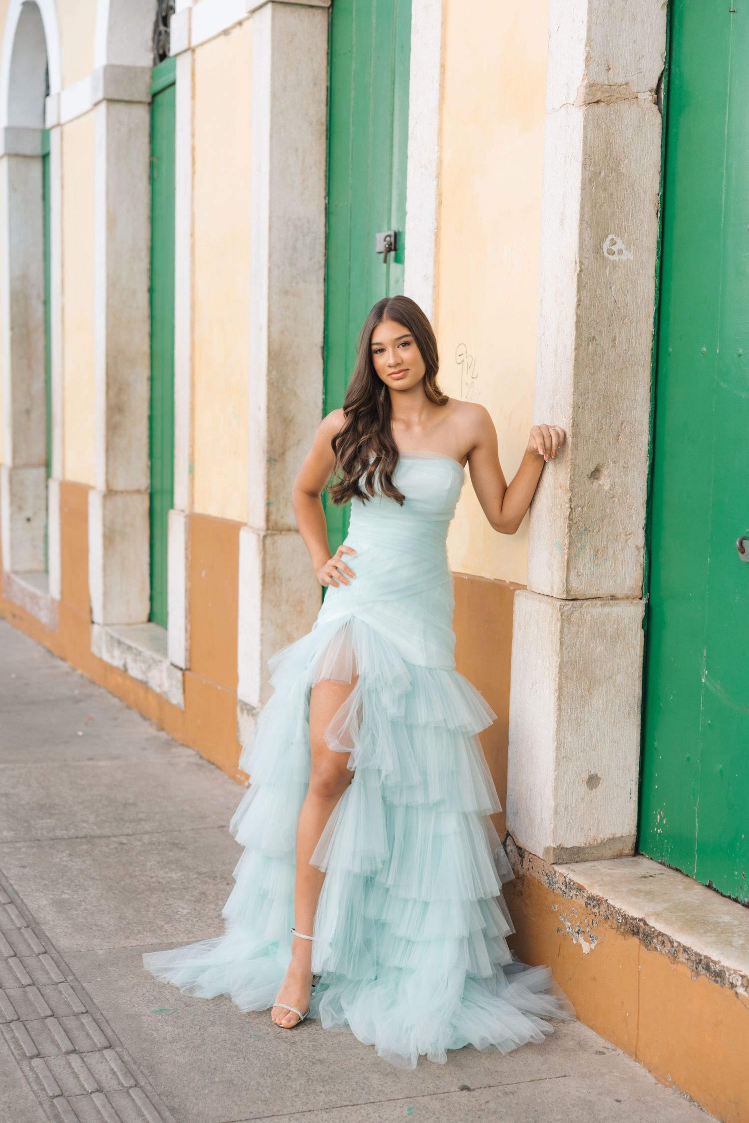 Elegant strapless mint green tulle gown with ruffled skirt against a backdrop of colorful colonial architecture.