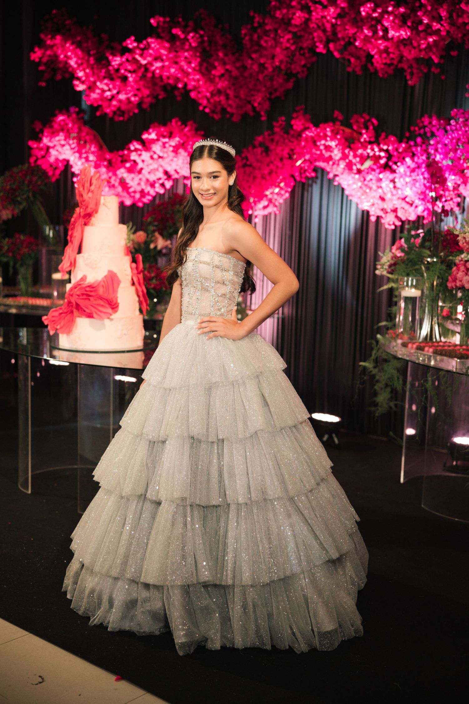 A glamorous silver ballgown with tiered tulle skirt photographed against a backdrop of bright pink cherry blossoms.