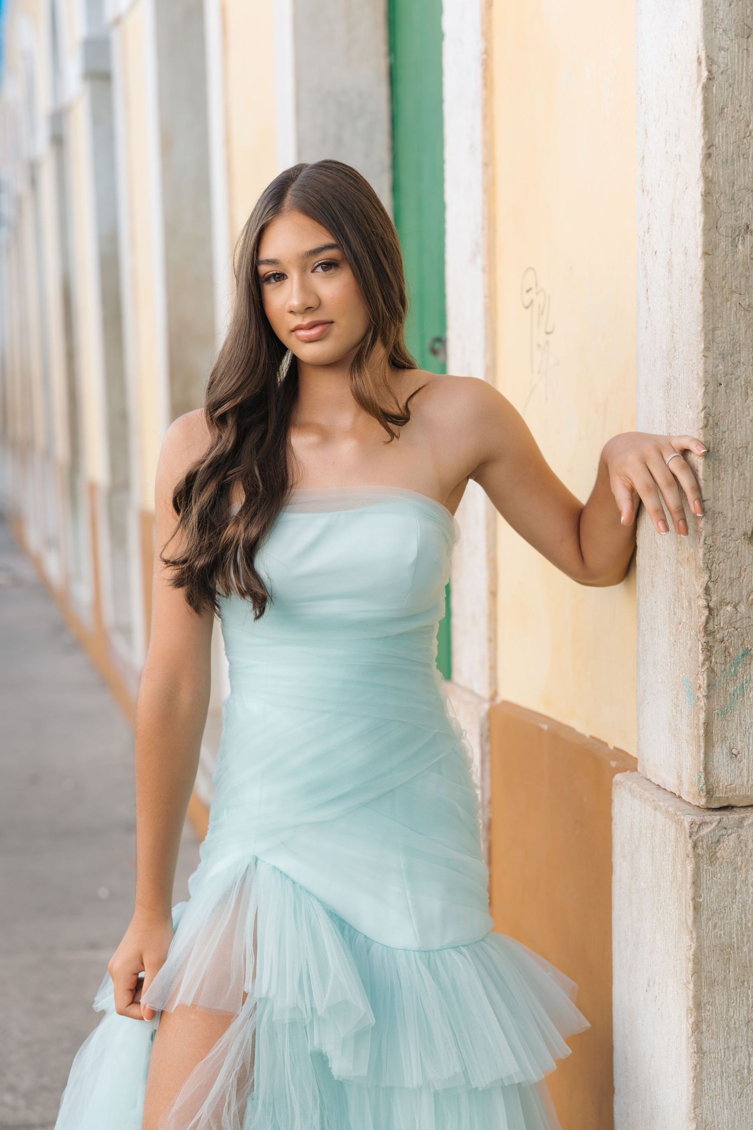 A strapless mint green tulle gown with ruffled layers is worn in an elegant outdoor setting with white columns.