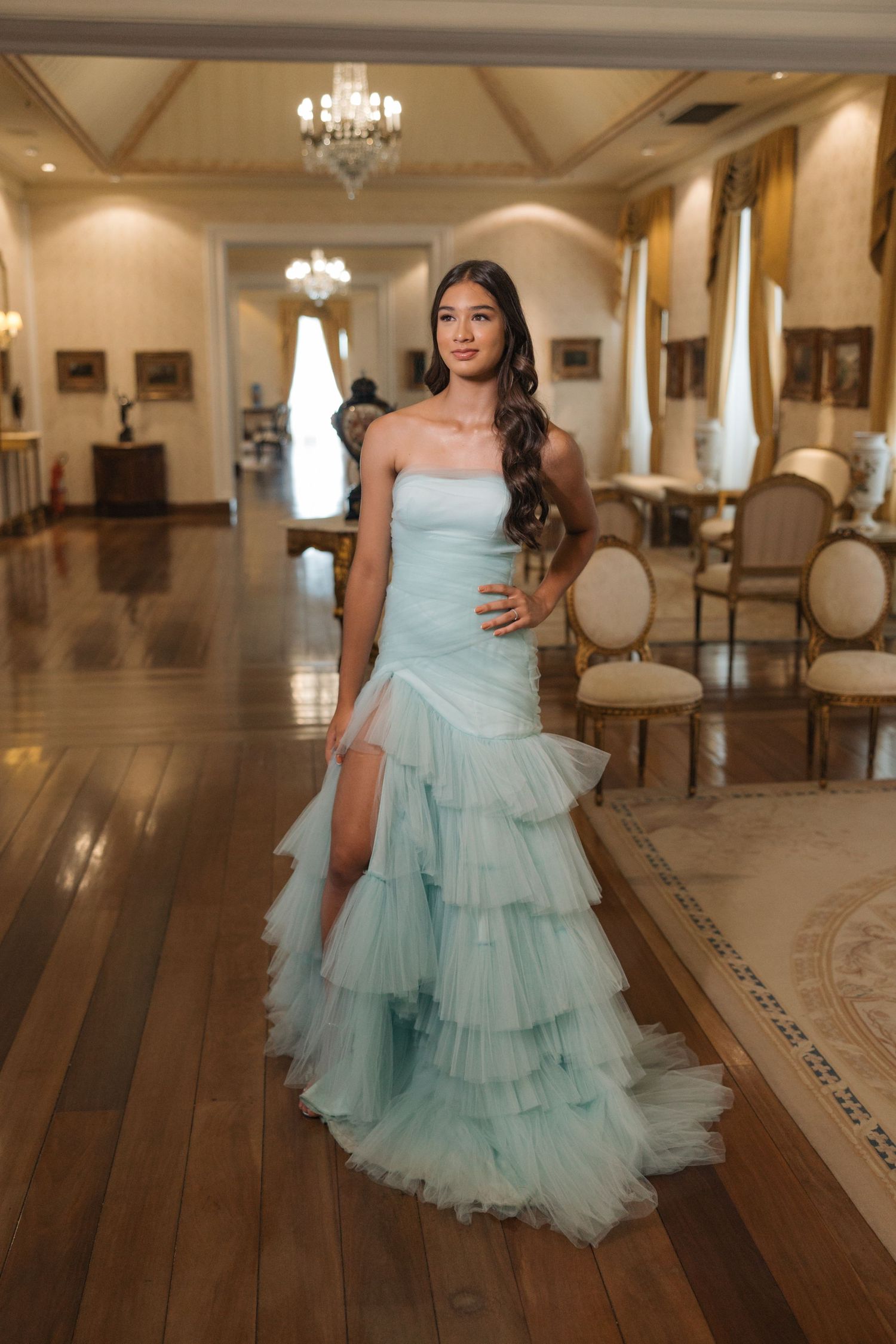 A stunning light blue tulle gown with tiered ruffles photographed in an elegant ballroom with chandeliers.