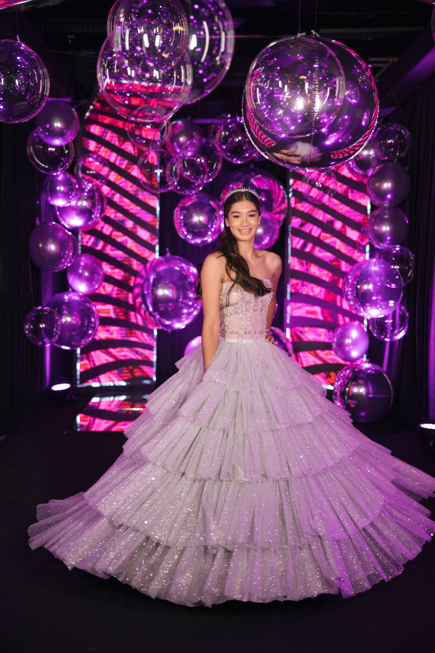 Sparkling silver ballgown showcased with purple balloon decor and neon pink lighting effects.