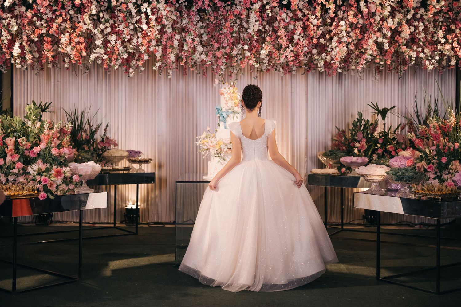 A wedding dress silhouette against a romantic backdrop of pink floral arrangements and soft lighting.