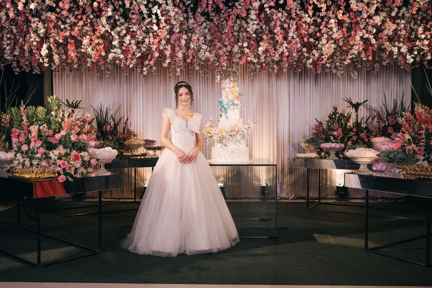A wedding venue decorated with pink floral arrangements and a beautiful white ballgown on display.