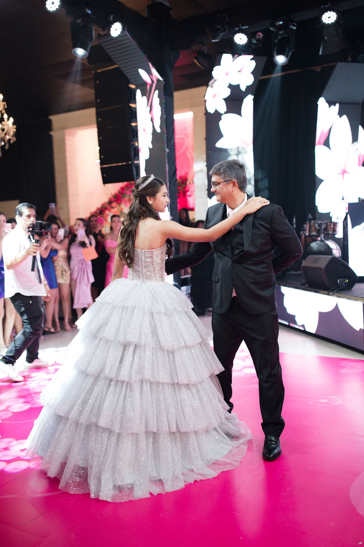 A quinceañera celebration showing a dance moment on a red-lit dance floor with decorative backdrops.