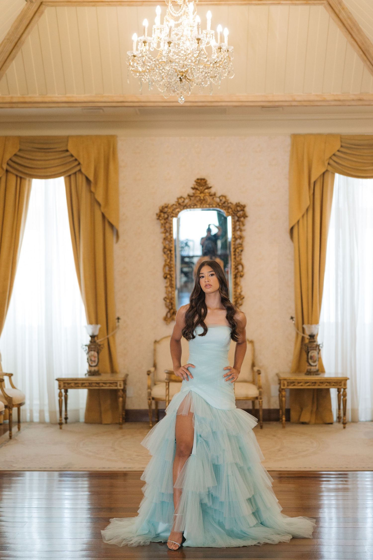 Luxurious mint ball gown photographed in an opulent room with crystal chandelier and gold-framed mirror.
