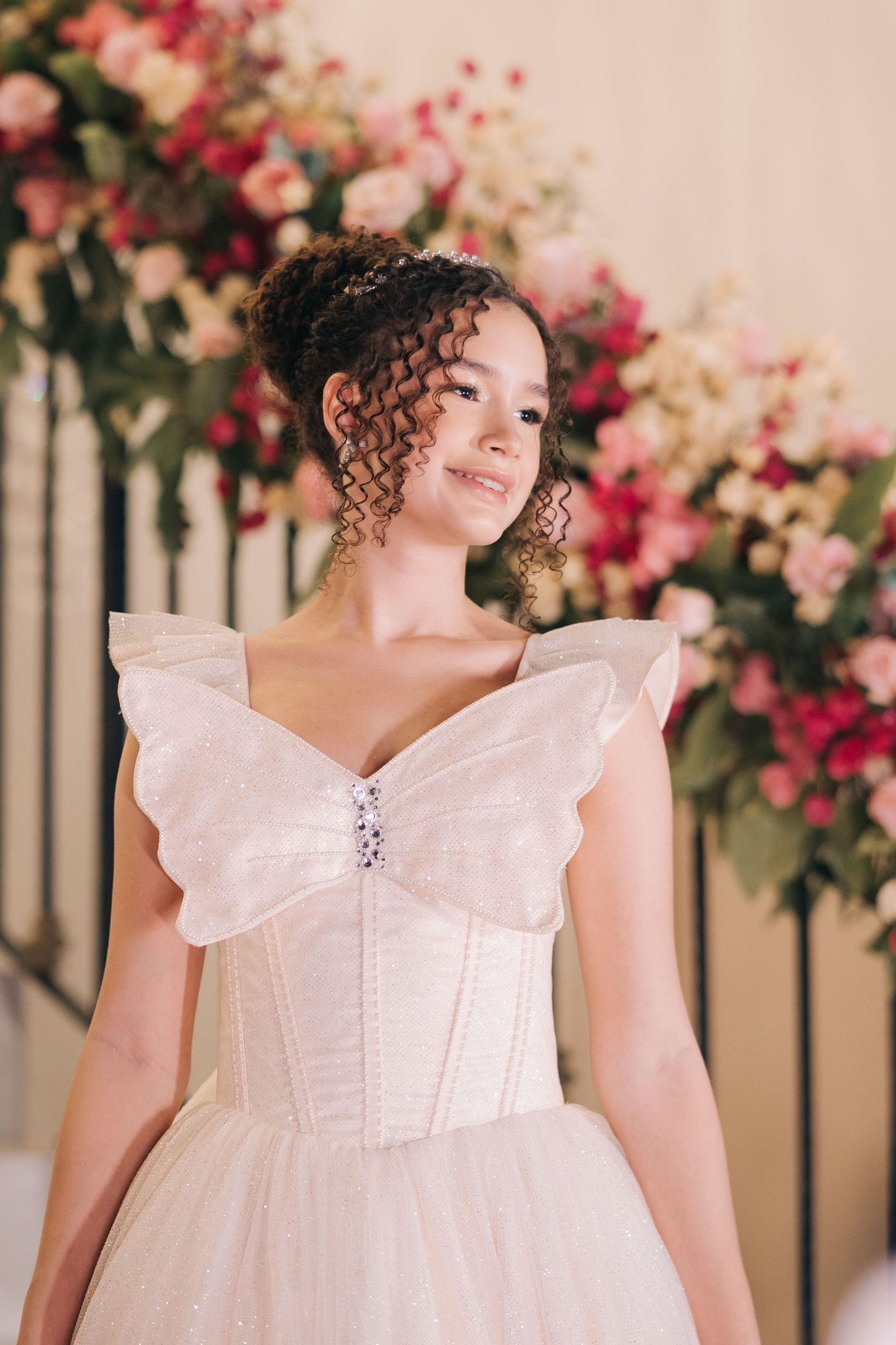 Princess-style wedding dress with butterfly wing-like details and delicate embellishments against floral backdrop.