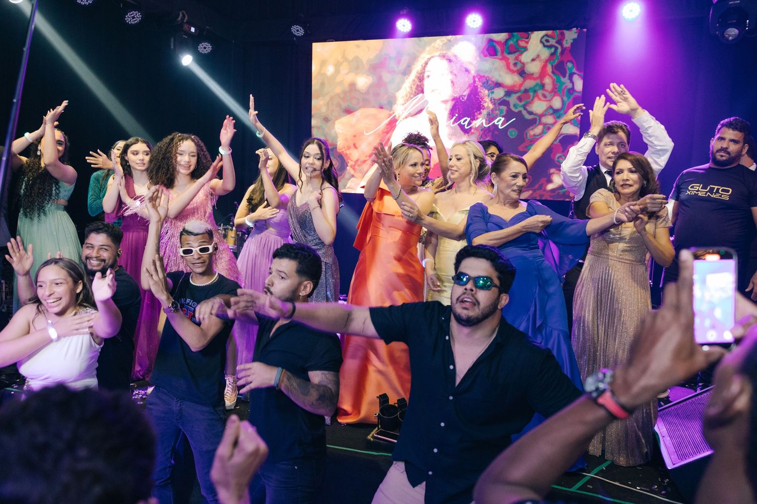 Lively party crowd dancing and celebrating under colorful stage lights.