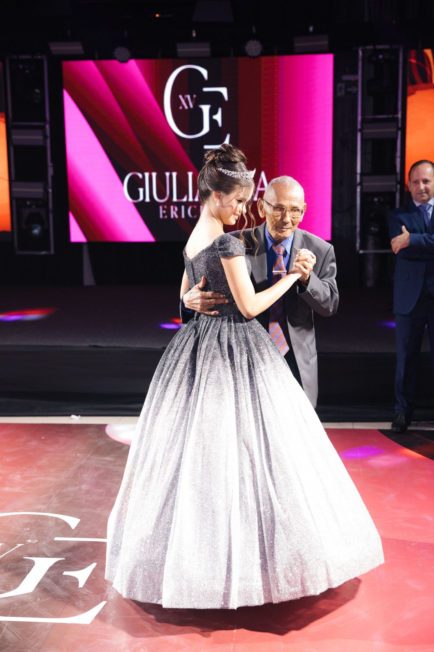 A celebratory dance moment on a red-lit stage with a glowing pink backdrop displaying the Giulia logo.