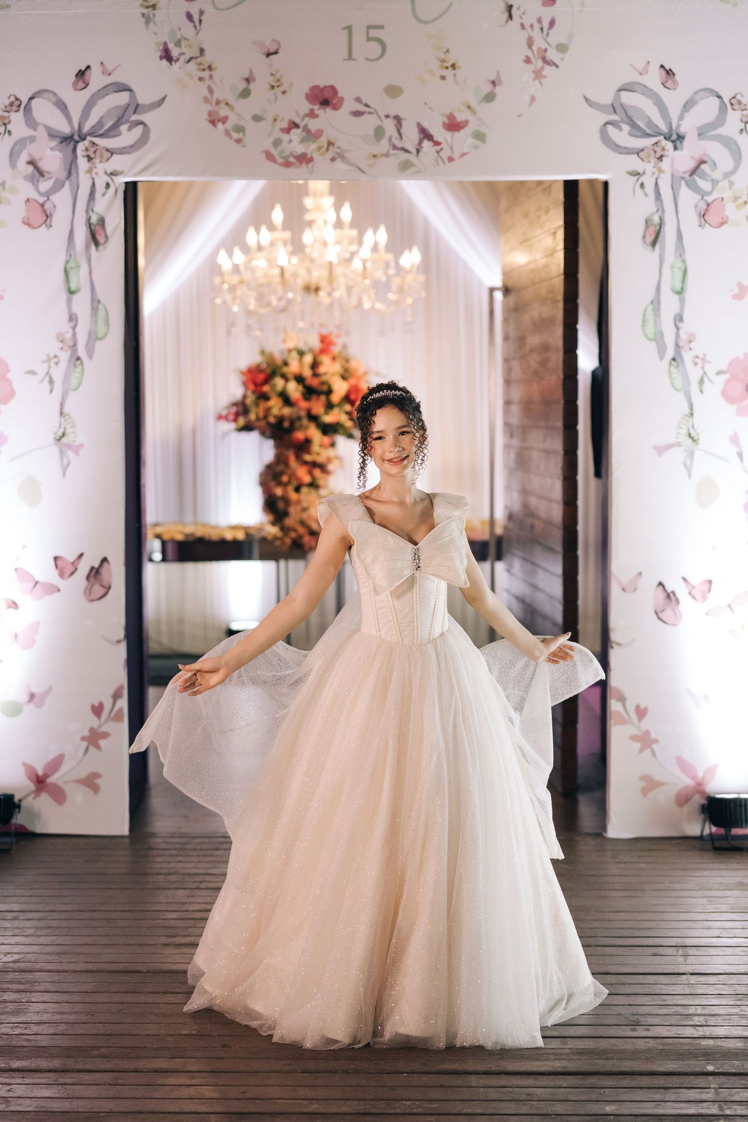 An elegant ballgown wedding dress captured in a venue with floral wallpaper and crystal chandelier.