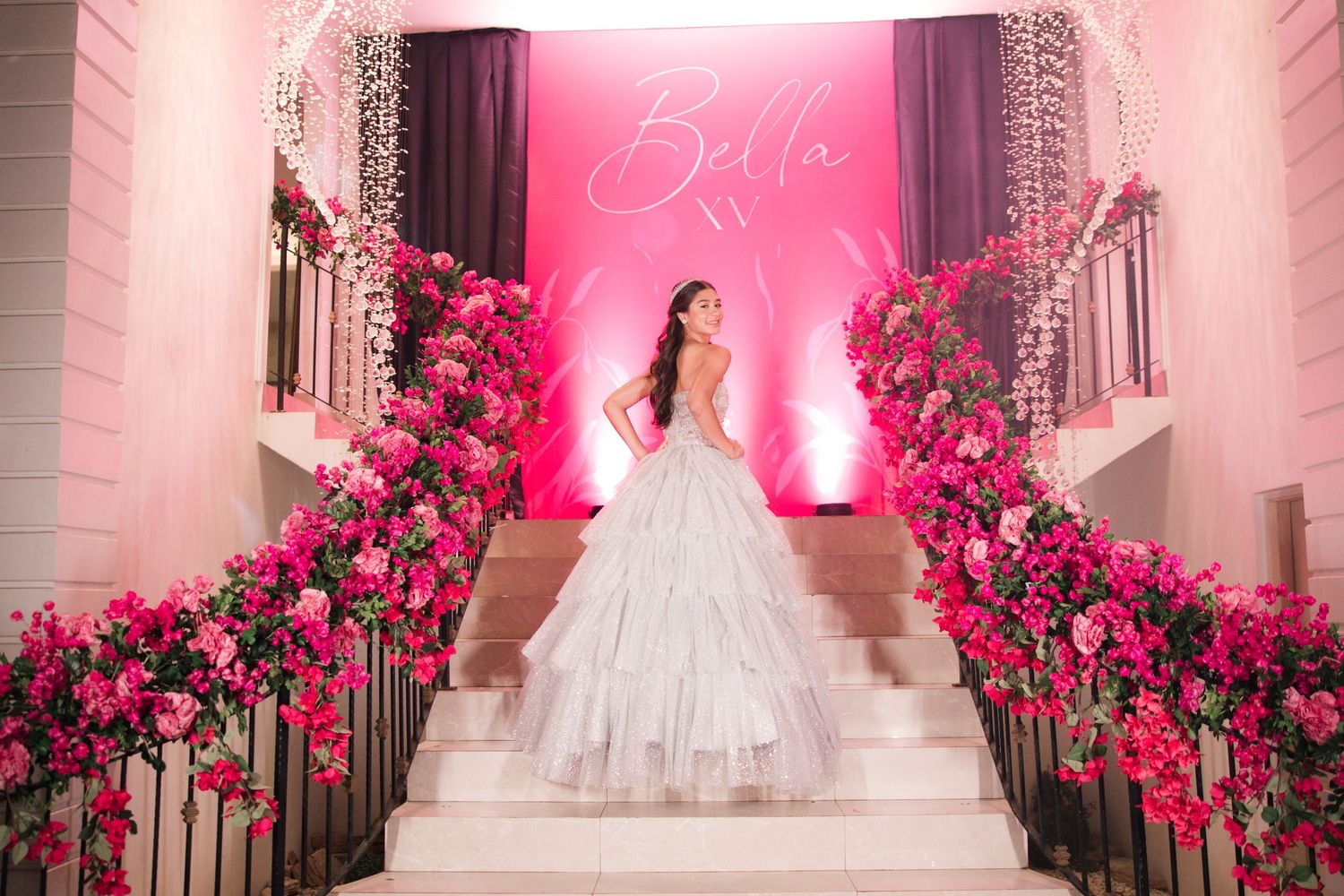 Elegant white staircase entrance adorned with pink roses and dramatic lighting for a special celebration.