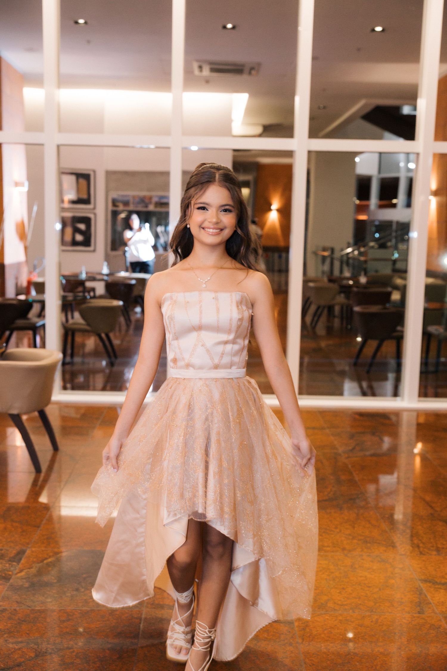 Elegant high-low dress with layered tulle skirt shown against modern glass wall interior.