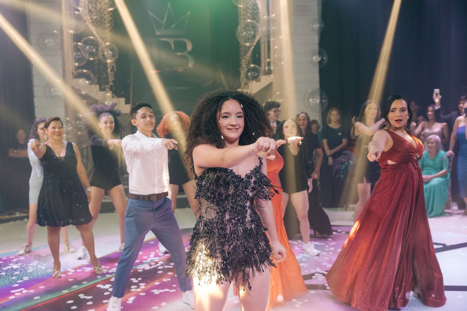 People dancing and celebrating at a vibrant party with disco lights and confetti on the dance floor.