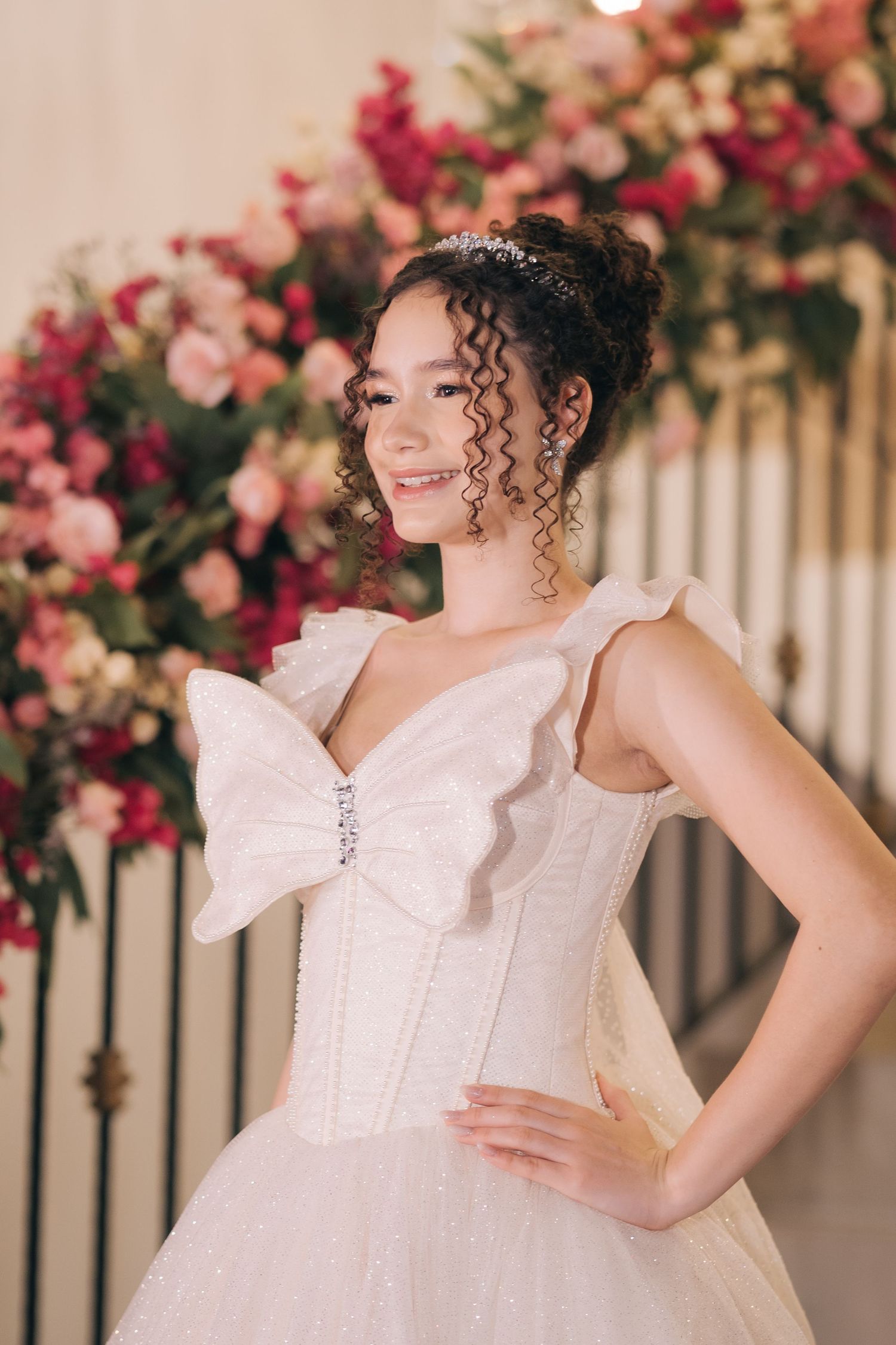 A bride in an elegant white dress with bow detail poses against a backdrop of pink and coral flowers.