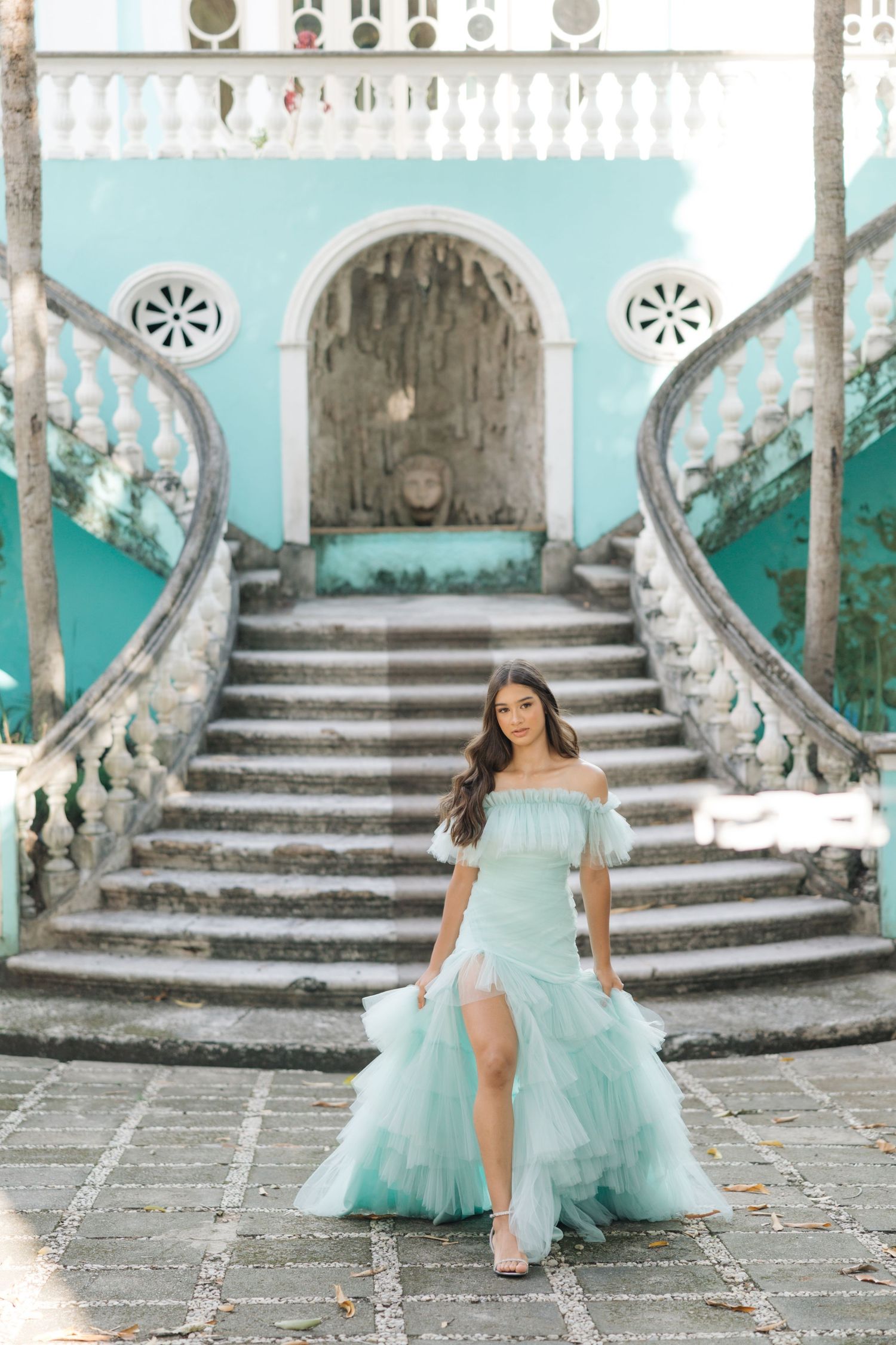Ethereal turquoise gown with flowing tulle skirt photographed on grand ornate staircase with vintage architecture.
