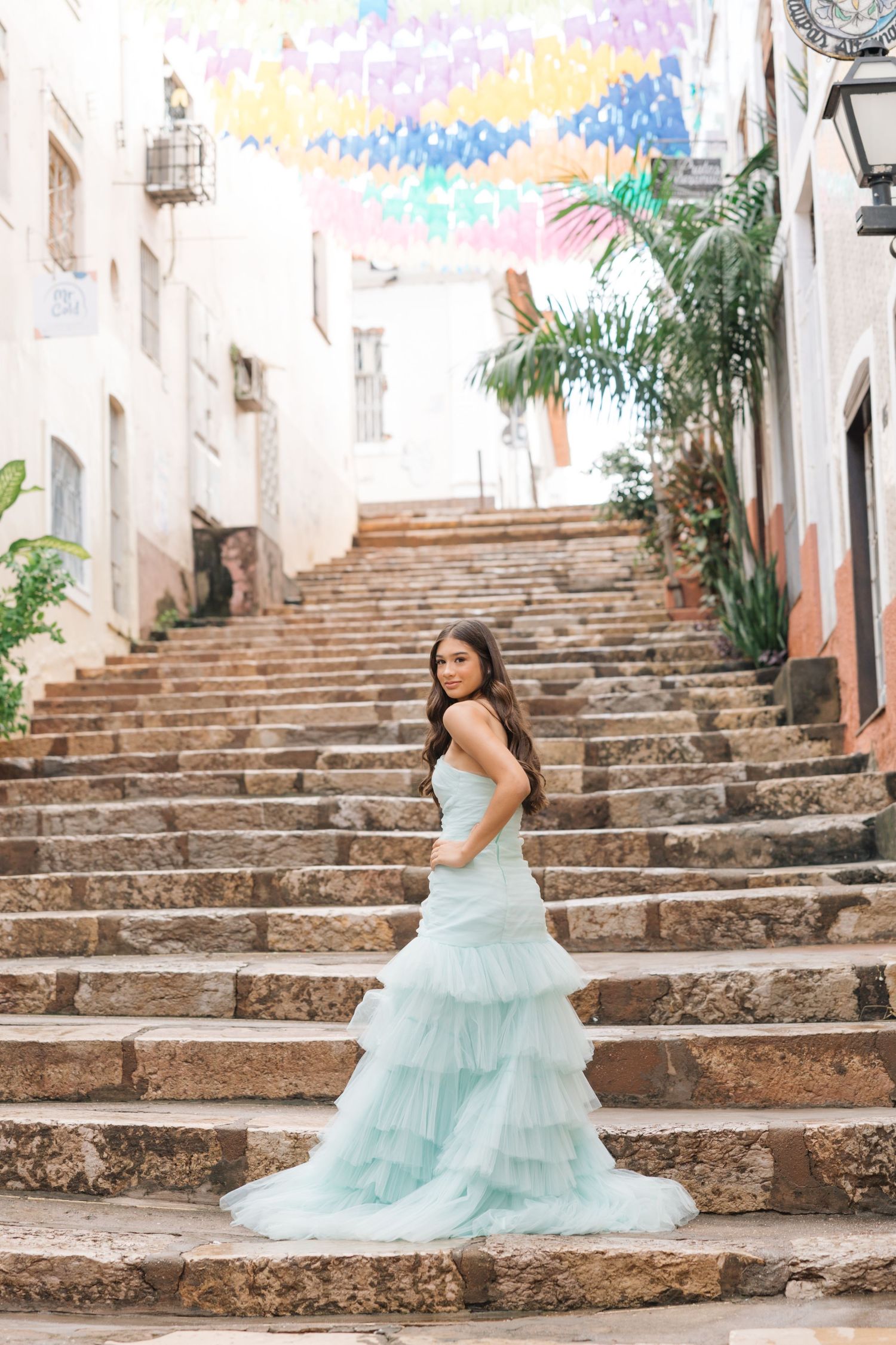 An elegant mint green ruffled gown stands out against historic stone steps and whitewashed walls.