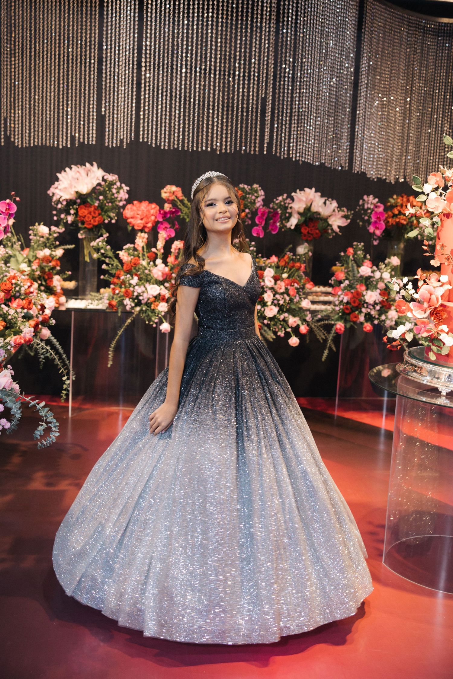 A stunning ombre ball gown transitions from navy to silver glitter against a backdrop of colorful floral arrangements.
