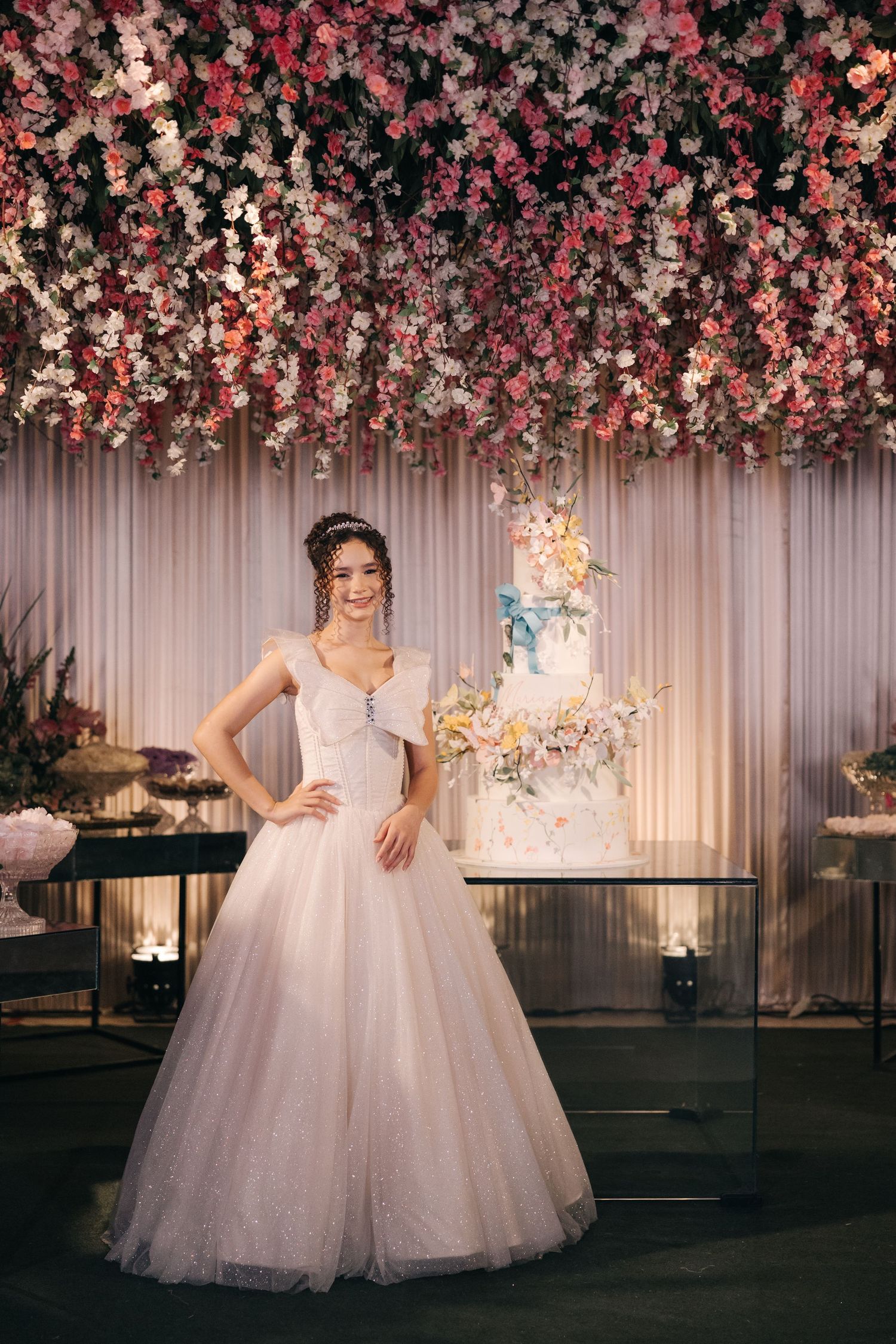 Elegant wedding scene with tiered cake and dramatic floral ceiling installation in pink and white.