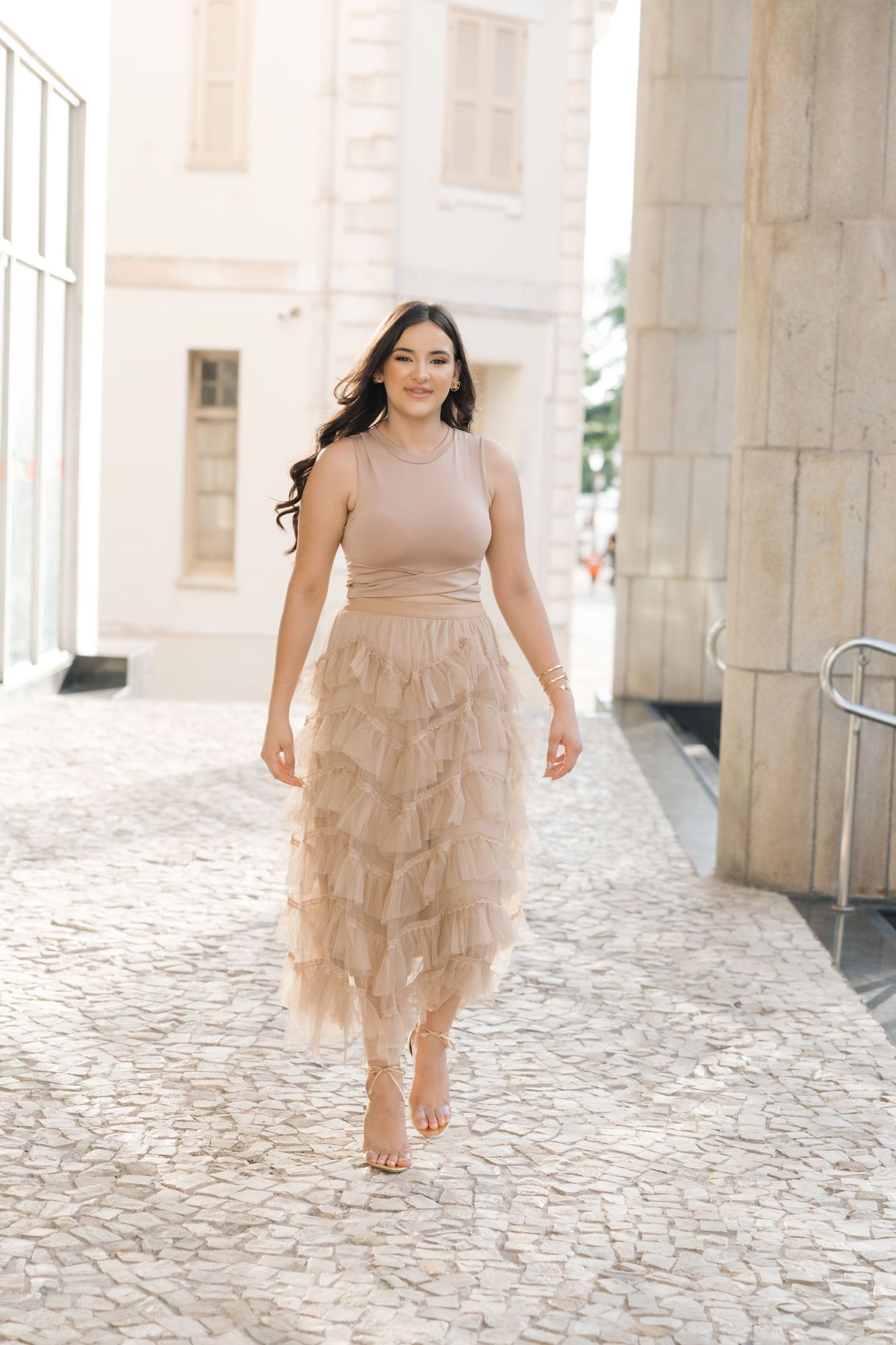 Beautiful beige ruffled tulle midi dress shown on cobblestone path near elegant stone columns.